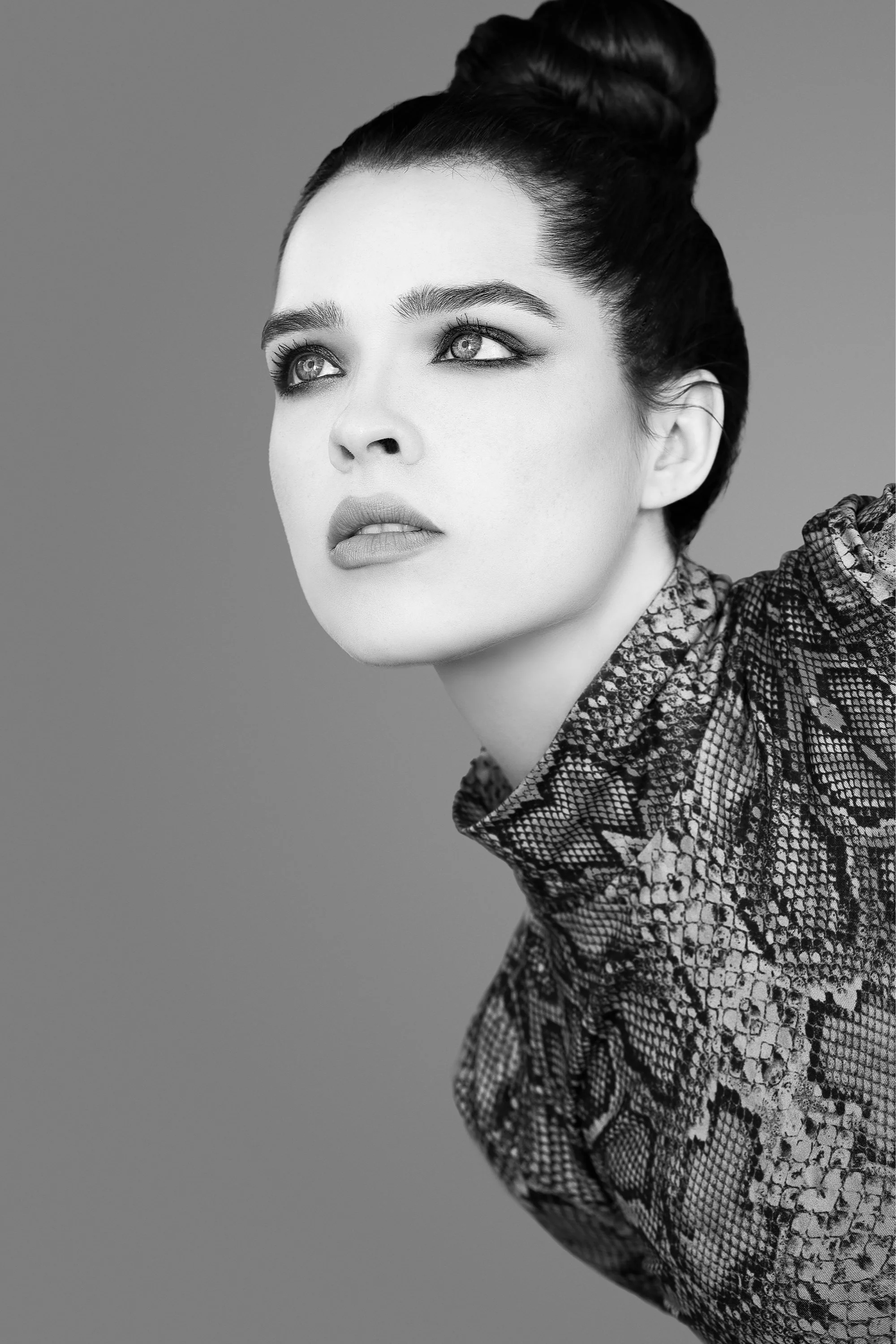 Black and white portrait of a woman with dark hair styled in an updo, wearing a patterned top, looking slightly upward and to the left.