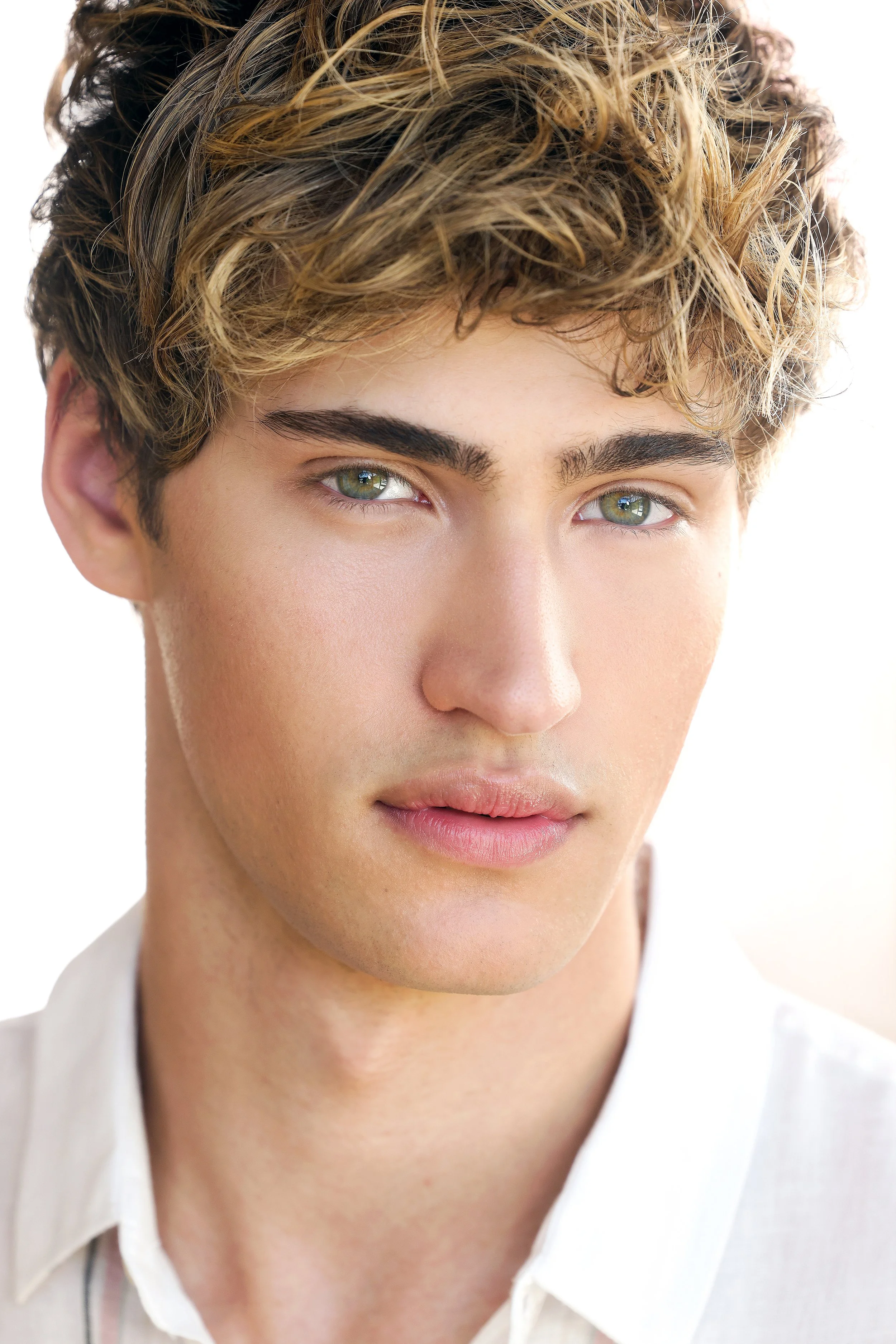 Close-up portrait of a young man with curly, light brown hair and piercing green eyes, wearing a white collared shirt.  Image by top Los Angeles photographer Kenneth Dolin. 