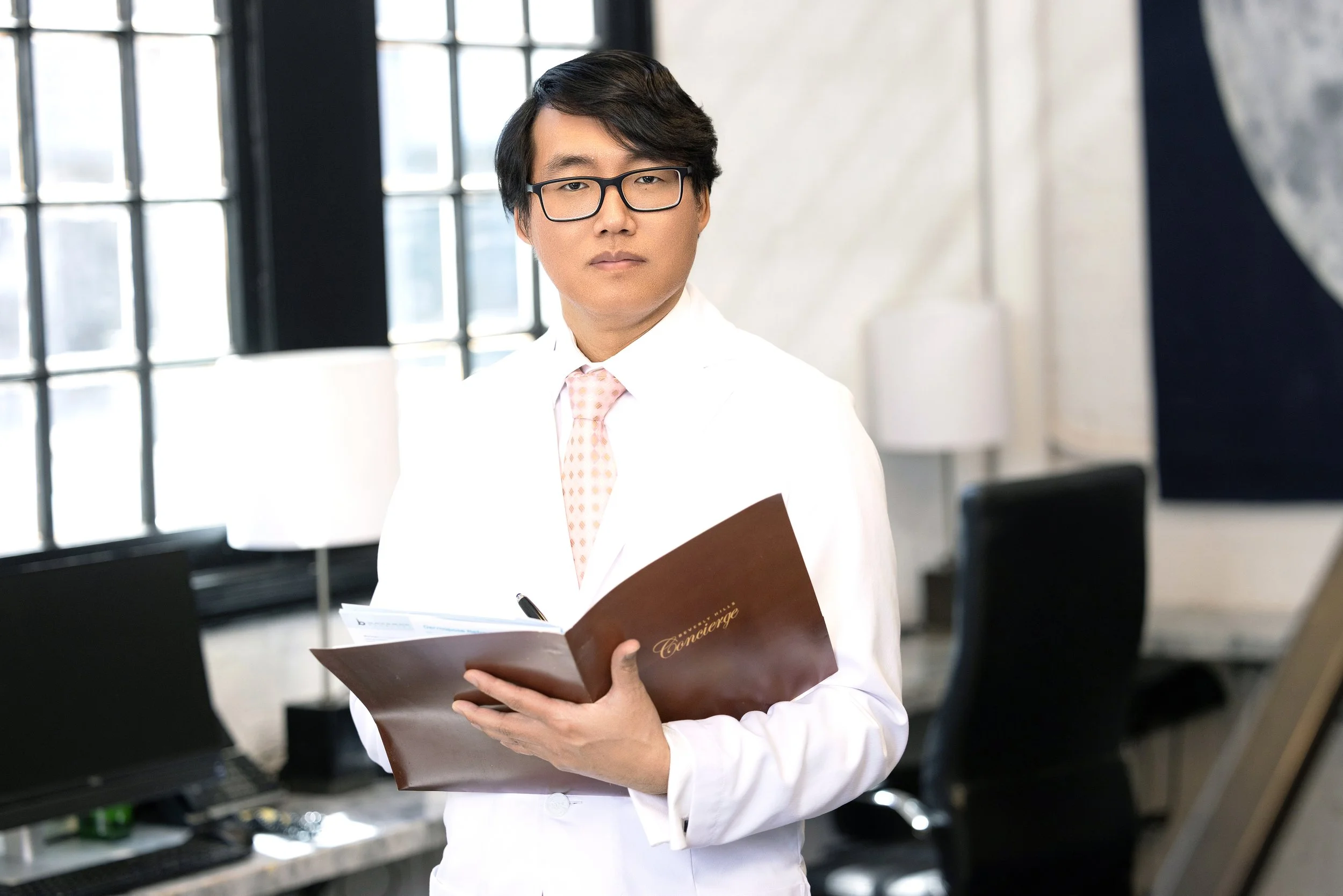 A man in a white shirt and glasses holding a brown concierge booklet in an office setting.