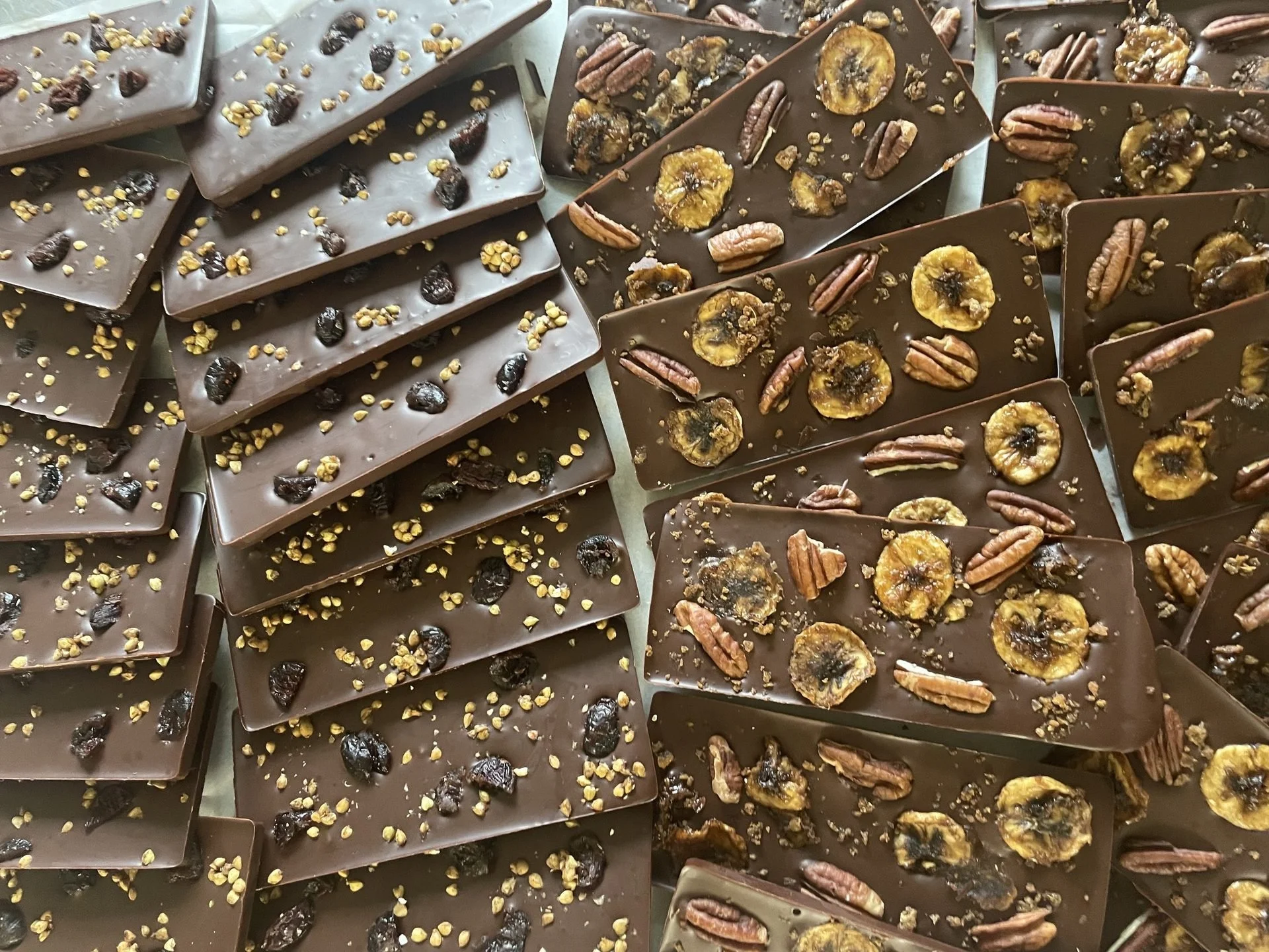 Assorted chocolate bars with various toppings including raisins, banana chips, walnuts, and nuts.