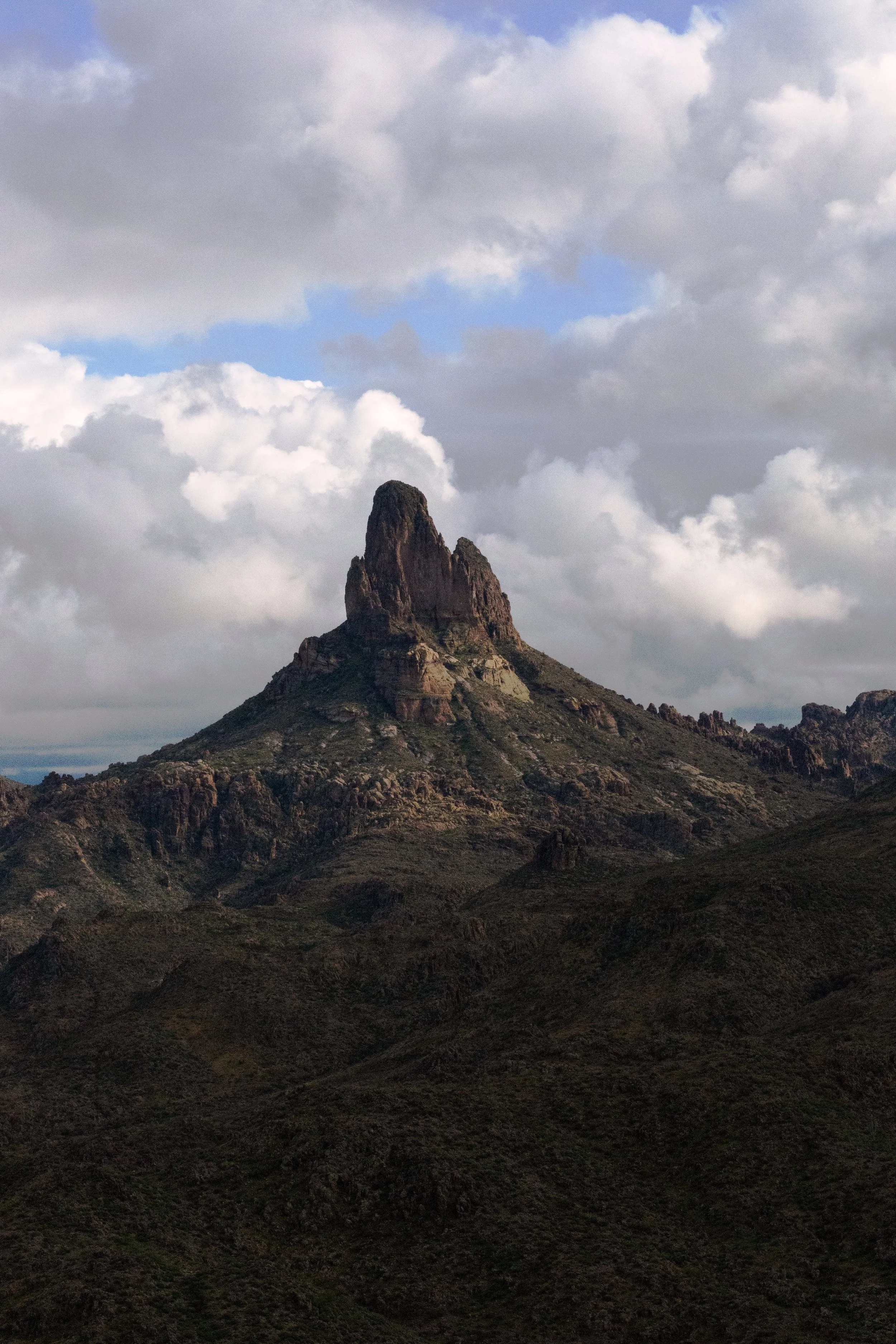 A rock formation in the desert mountains rising under a cloudy blue sky.