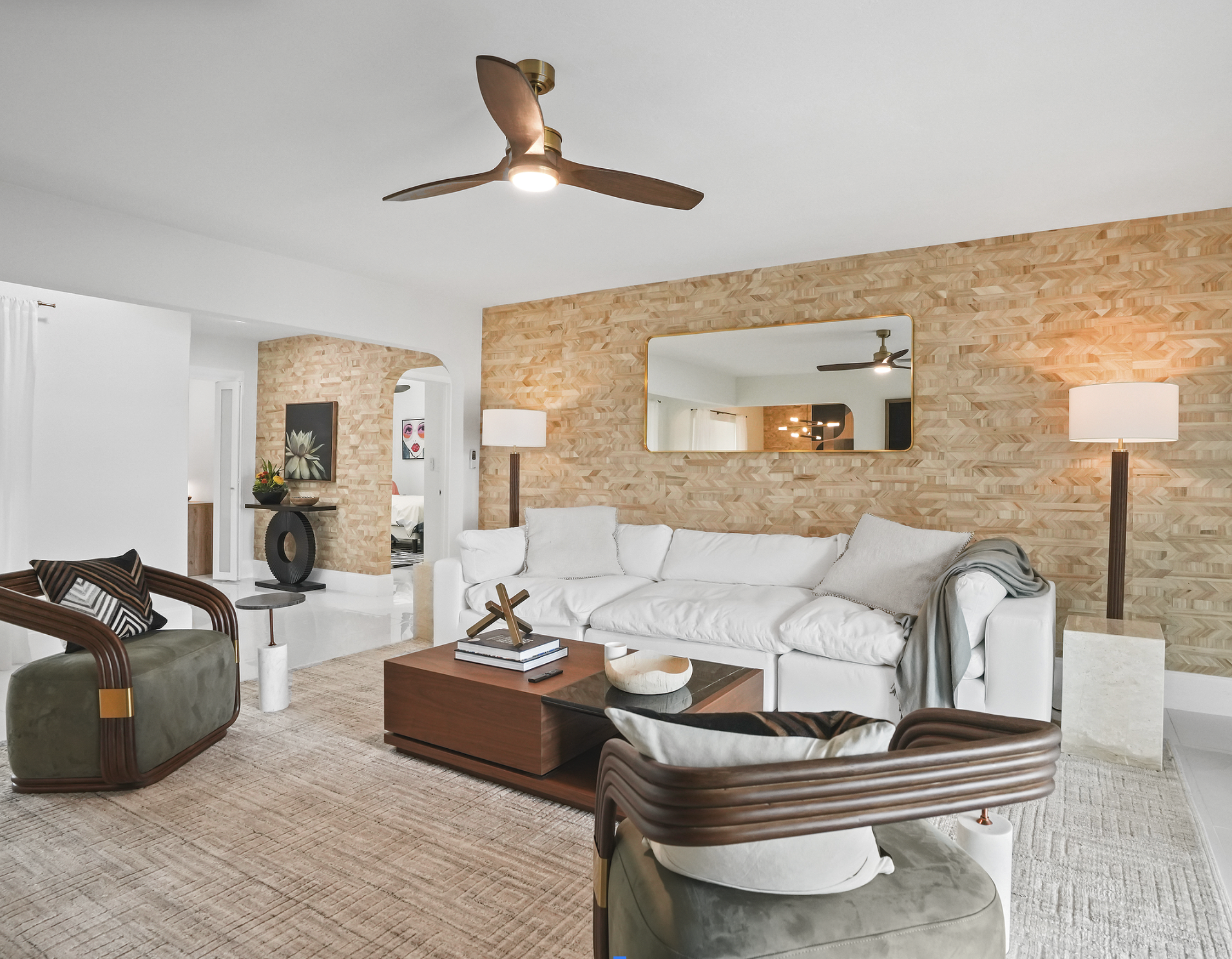 Wide view of Miami vacation rental living room with textured feature wall, white sofa, sculptural lounge chairs, and Tulum-inspired coastal styling.