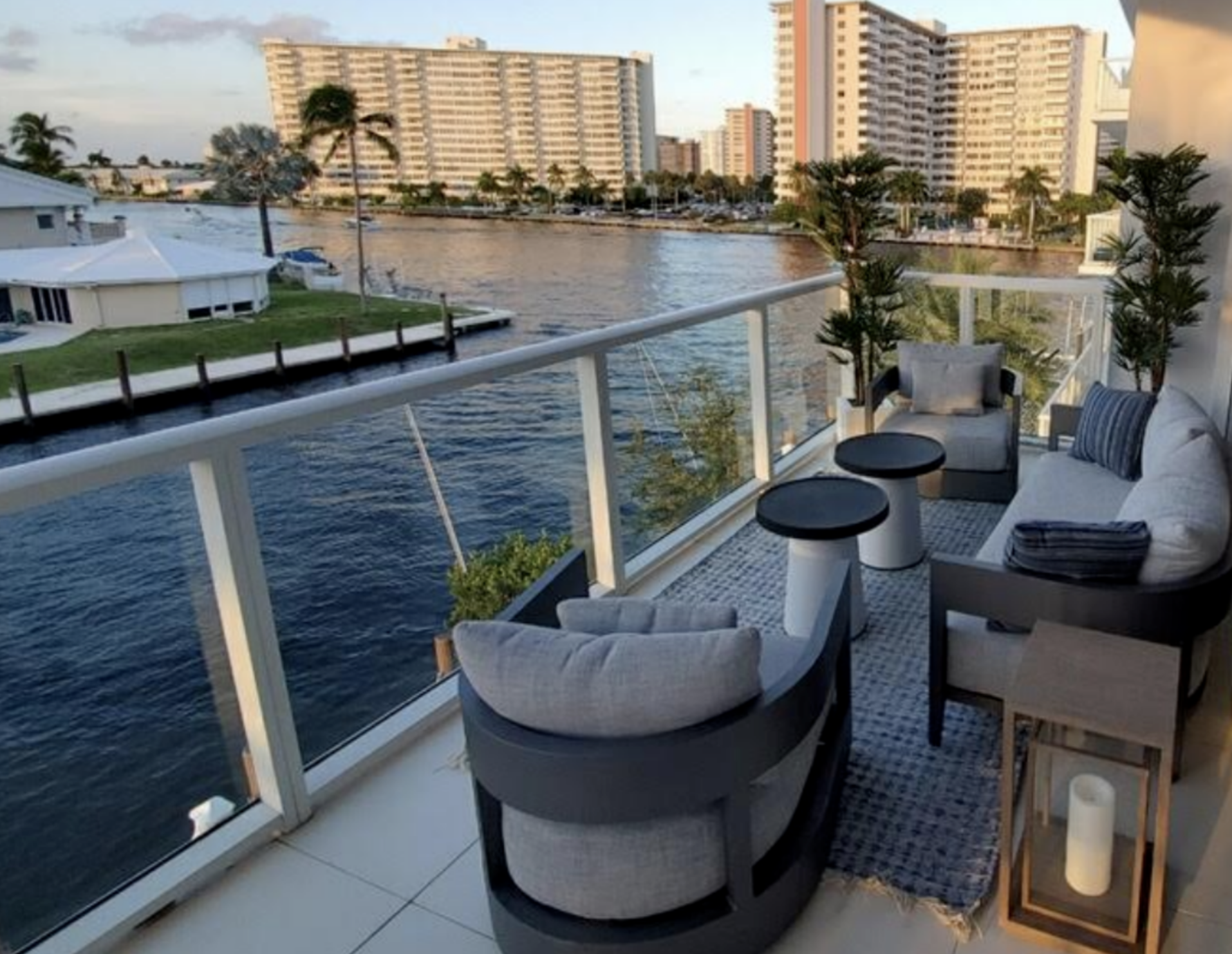 Fort Lauderdale penthouse wraparound balcony lounge with compact outdoor seating, layered textiles, and waterfront views, designed to maximize small space living with an urban coastal aesthetic for a well-traveled investor
