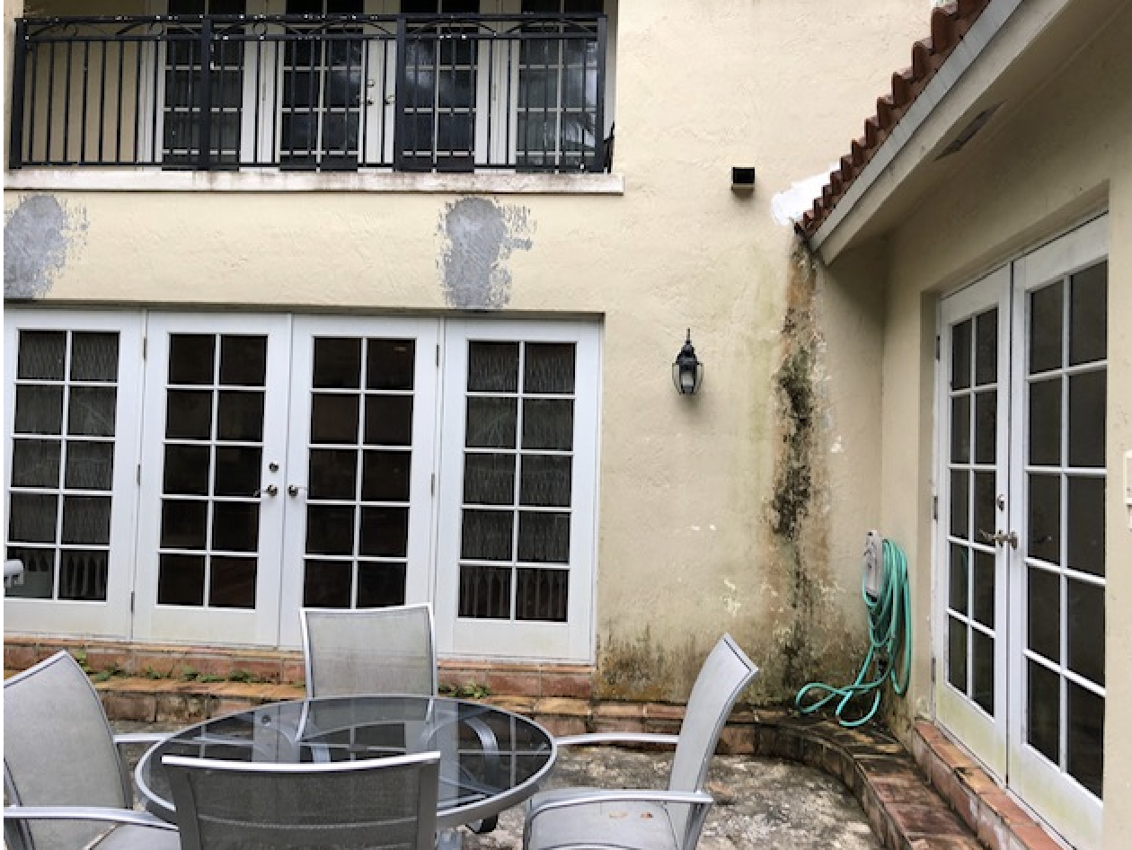 Exterior courtyard before renovation showing deteriorated stucco walls and water damage requiring repair, repointing, and mitigation prior to painting and new patio installation in Coconut Grove Miami home remodel.