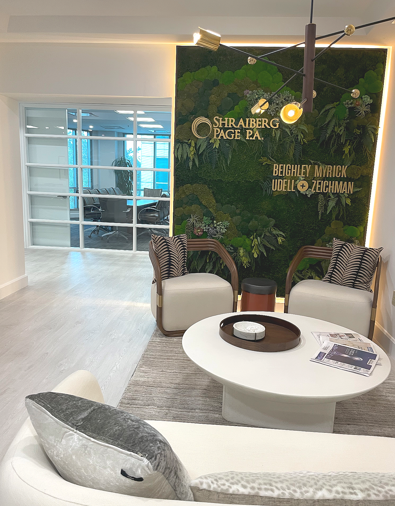 Luxury office lounge feature wall in Boca Raton showcasing a custom company logo sign with integrated LED backlighting on a preserved biophilic moss background, framed by freshly painted white window trim and ivory walls.