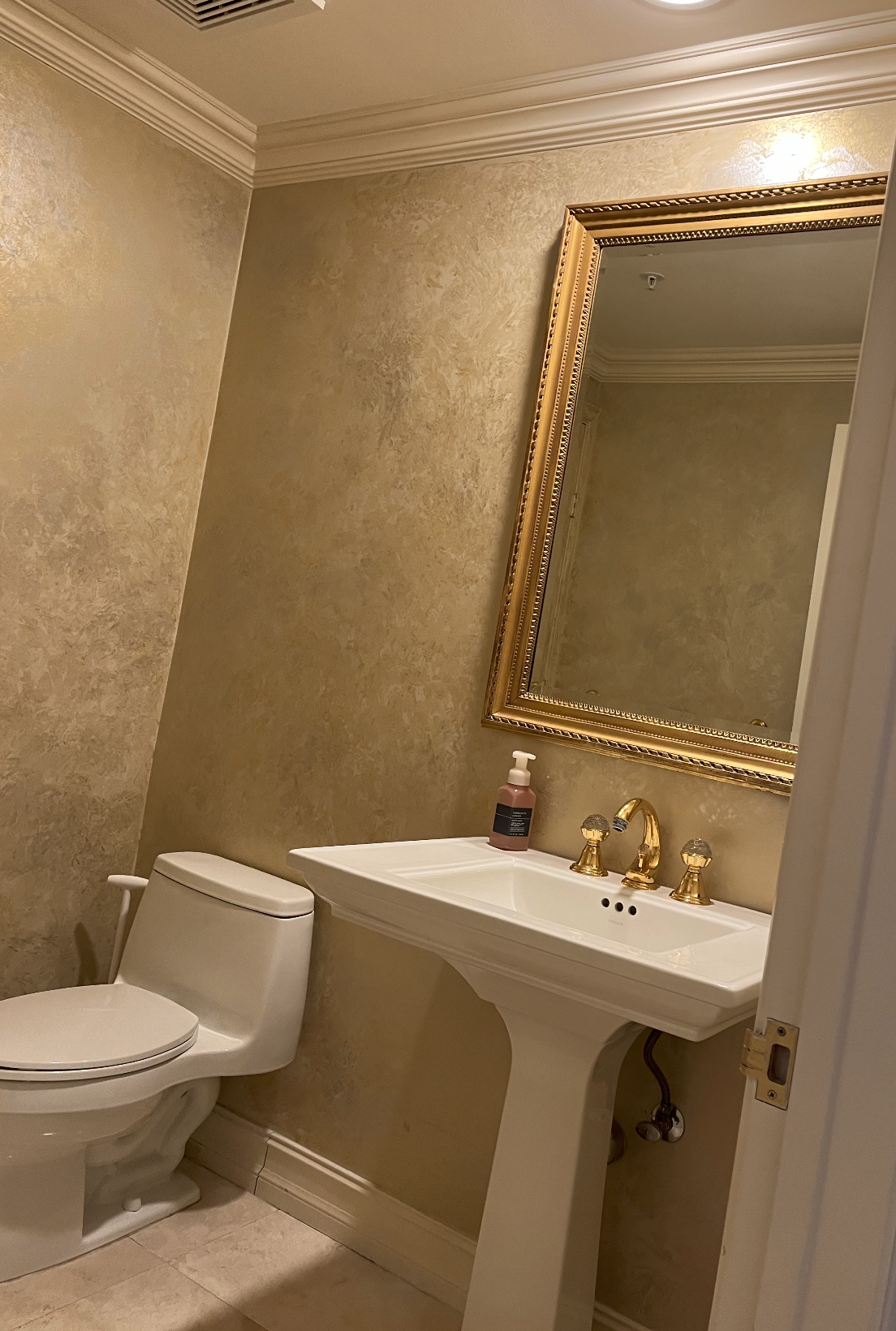 Before Hillsboro Beach condominium powder room with metallic faux-finish walls, pedestal sink, gold-framed mirror, and traditional fixtures before luxury renovation.