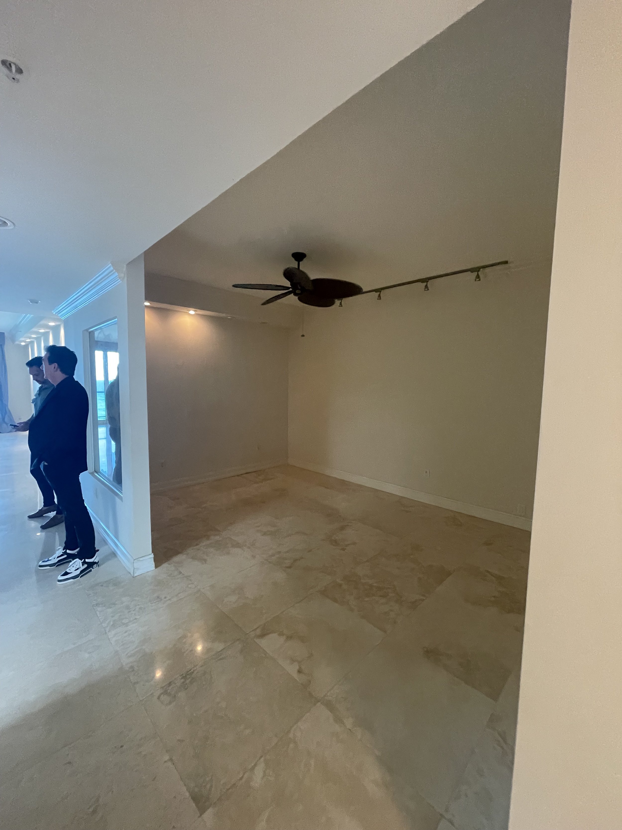 Before luxury condominium den remodel in Hillsboro Beach with enclosed layout, beige walls, polished stone flooring, and an underutilized secondary living space prior to renovation.
