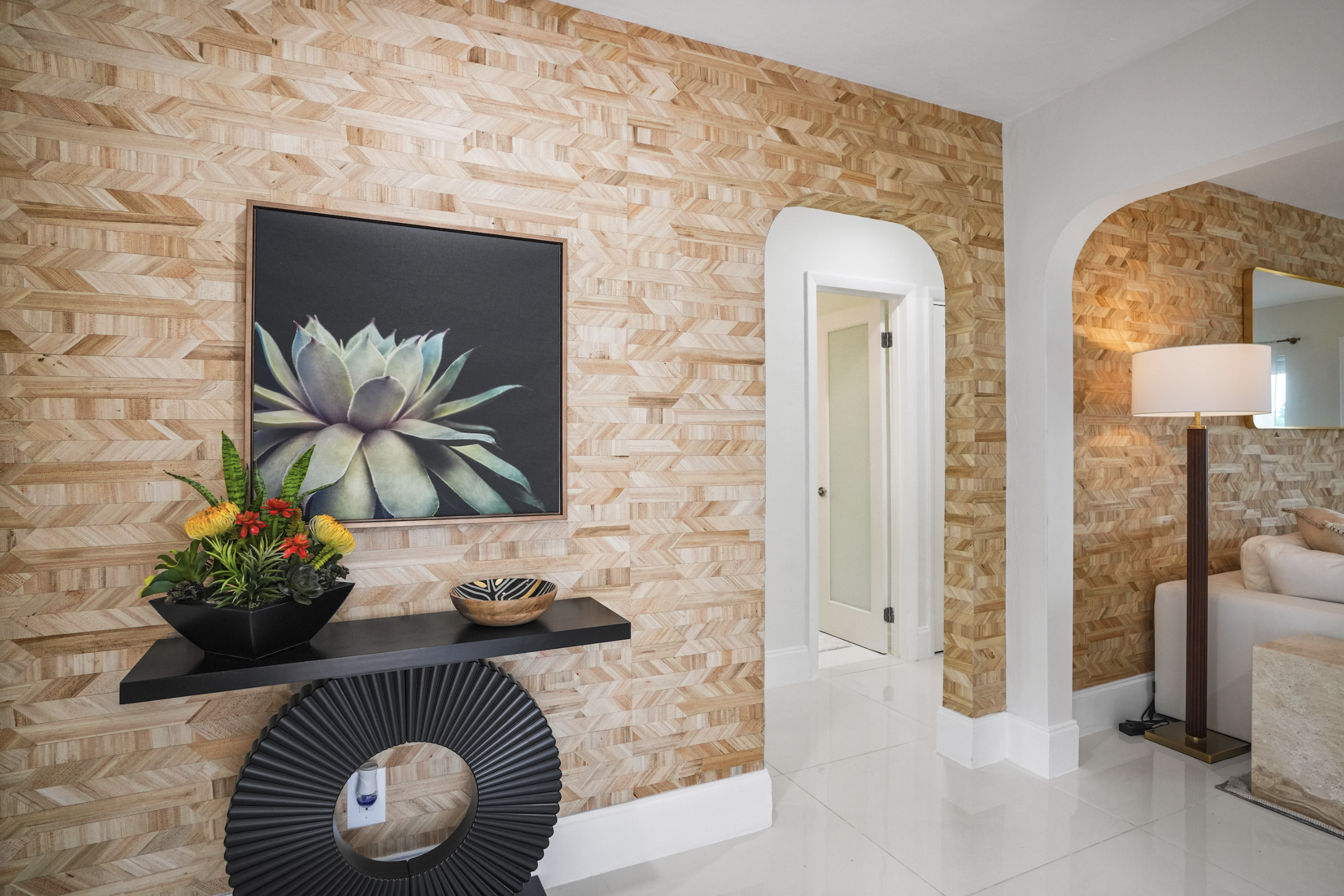 Textured feature wall and entry detail in Miami vacation rental with botanical artwork, floating console, arched opening, and Tulum-inspired interior styling.