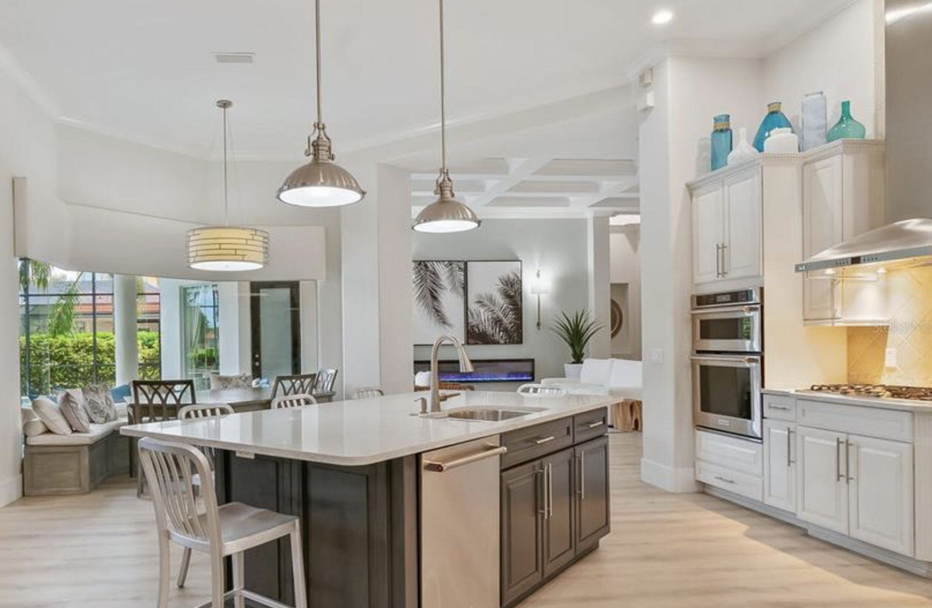 Updated open-concept kitchen remodel in Lakewood Ranch by Exclusively to Design featuring bright white cabinetry, updated coffered ceilings, modern barstools, and a streamlined island layout.