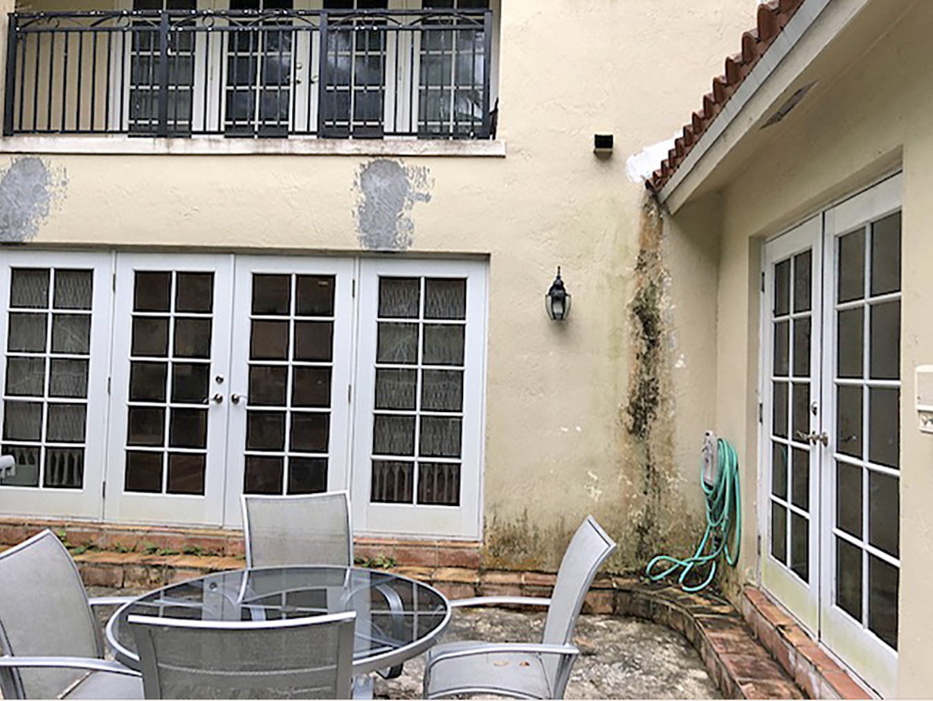 Exterior patio before renovation showing deteriorated stucco, outdated terrace flooring and weathered walls prior to home renovation by Exclusively To Design