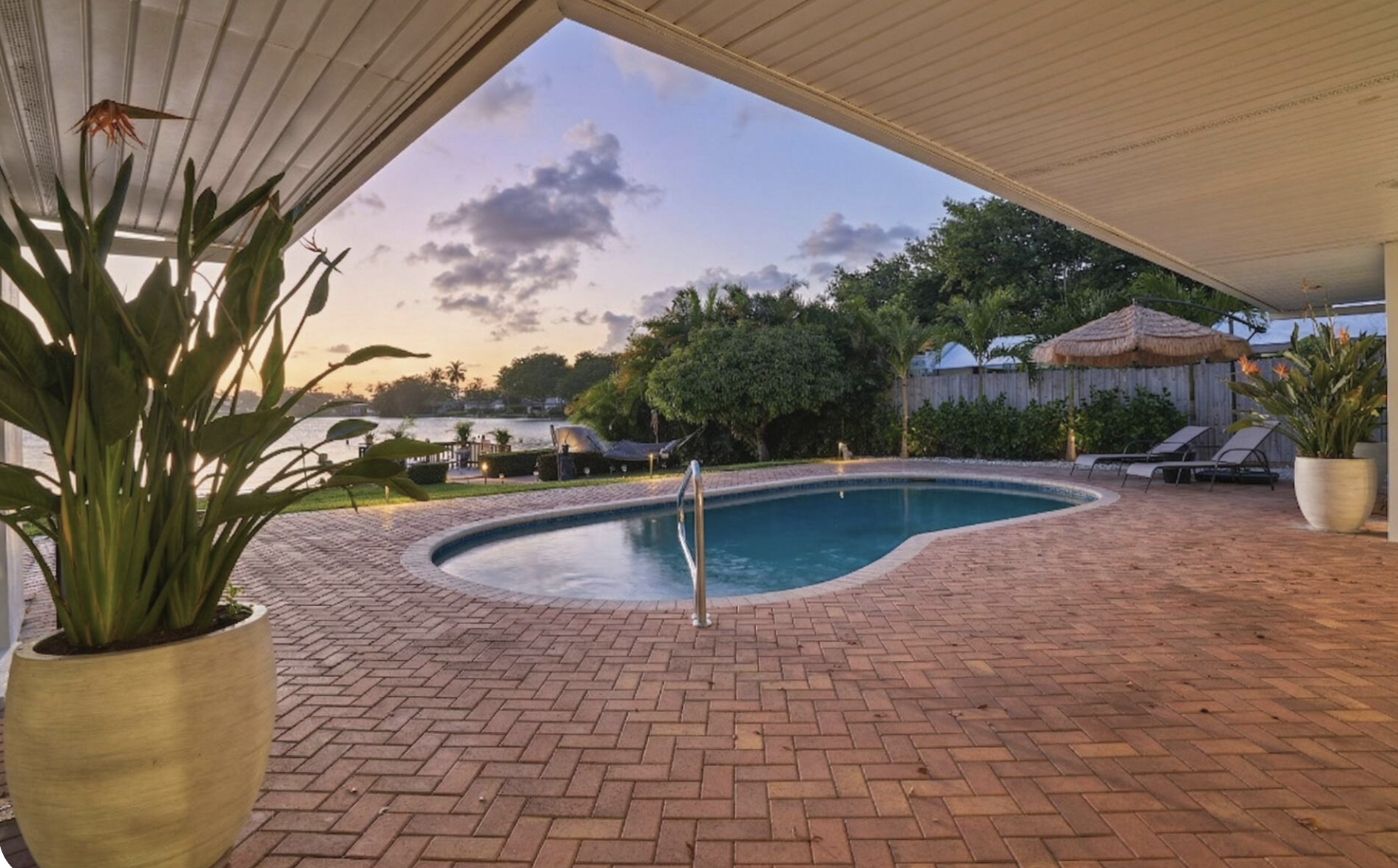 Pool patio in Miami vacation rental with bird of paradise planters, waterfront view, lounge chairs, and resort-style outdoor living.