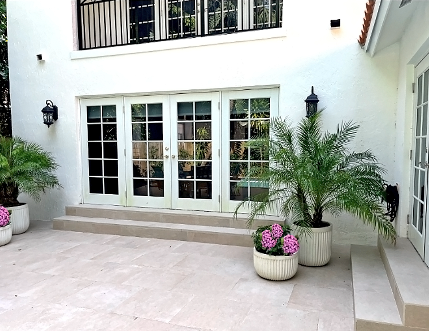 Exterior courtyard and terrace after home renovation featuring restored stucco facade, upgraded patio flooring and refreshed outdoor living space by Exclusively To Design