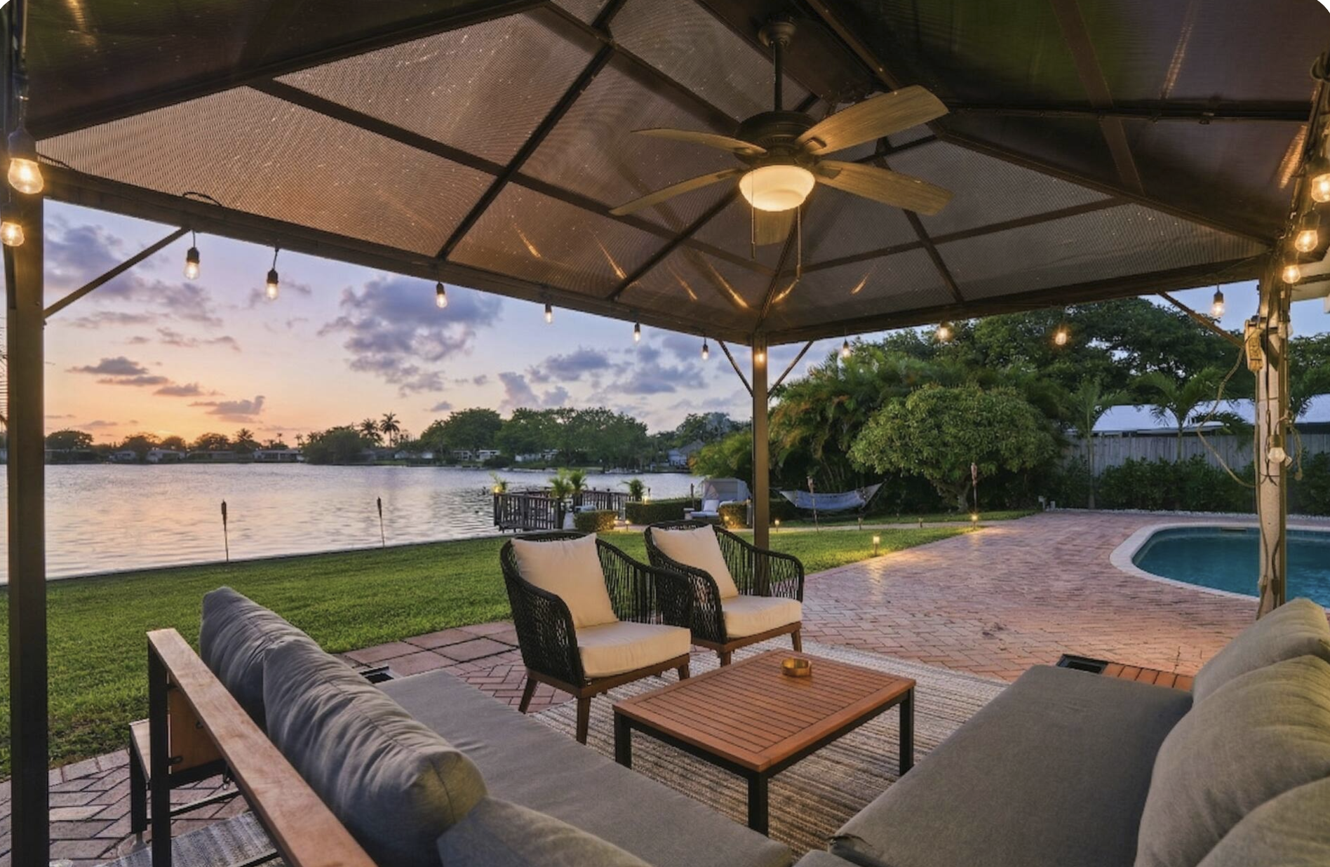 Pergola lounge area in Miami vacation rental with waterfront view, outdoor seating, string lights, and relaxed Tulum-inspired styling.
