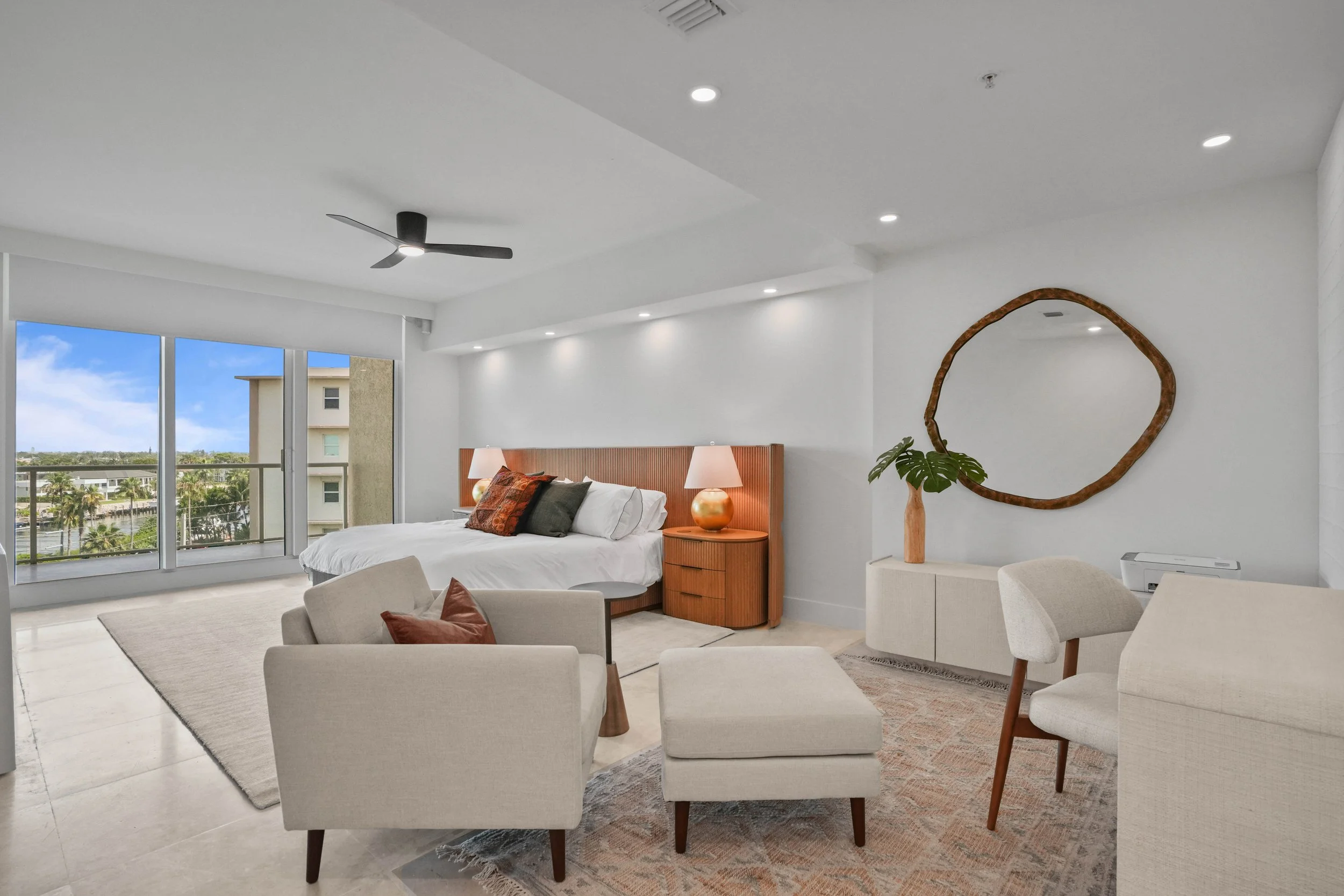 After Hillsboro Beach luxury primary bedroom remodel featuring a custom walnut headboard wall, integrated nightstands, layered seating area, recessed LED cove lighting, and panoramic Intracoastal Waterway views.