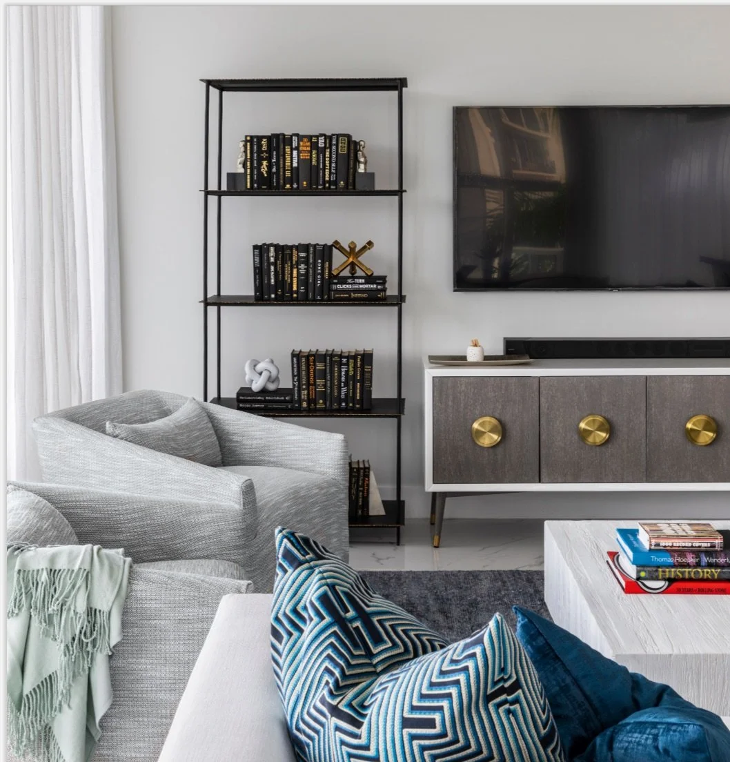 Fort Lauderdale penthouse living room detail with curated black library shelving, gold and silver accents, textured neutral seating, and geometric accent pillows reflecting an urban coastal aesthetic for a well-traveled investor
