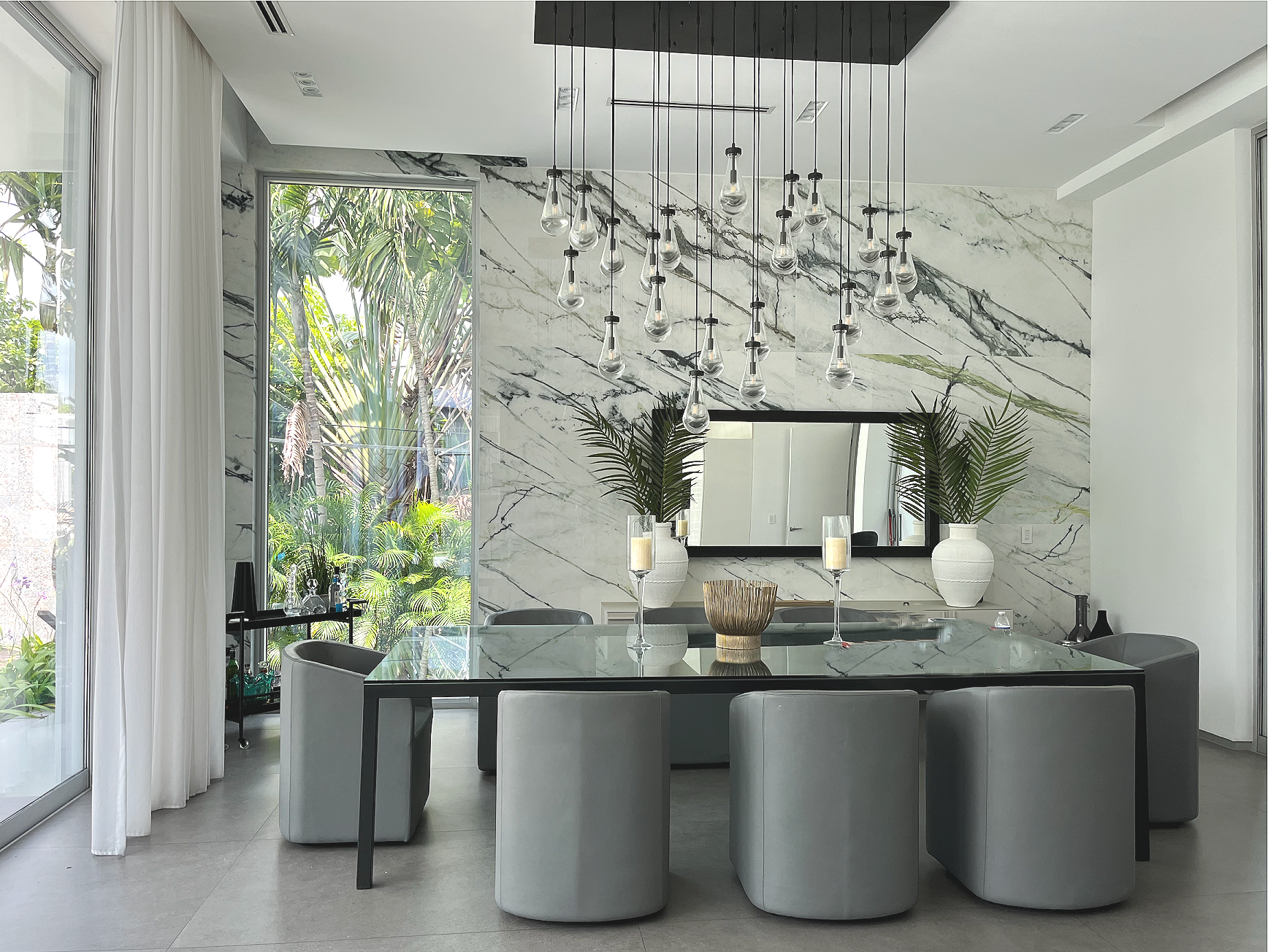 Miami Beach dining area with green Calacatta marble wall, pendant lighting, and tropical garden view