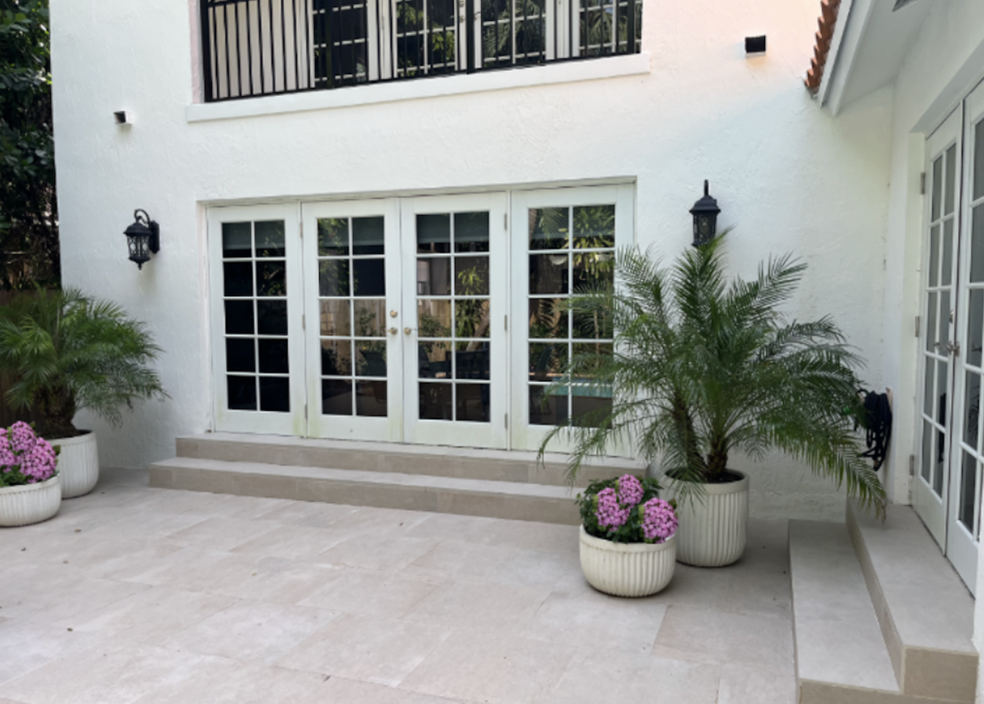 Exterior courtyard renovation with porcelain patio, French doors, landscape planters, and architectural lighting in a Coconut Grove Miami luxury home remodel by Exclusively To Design.