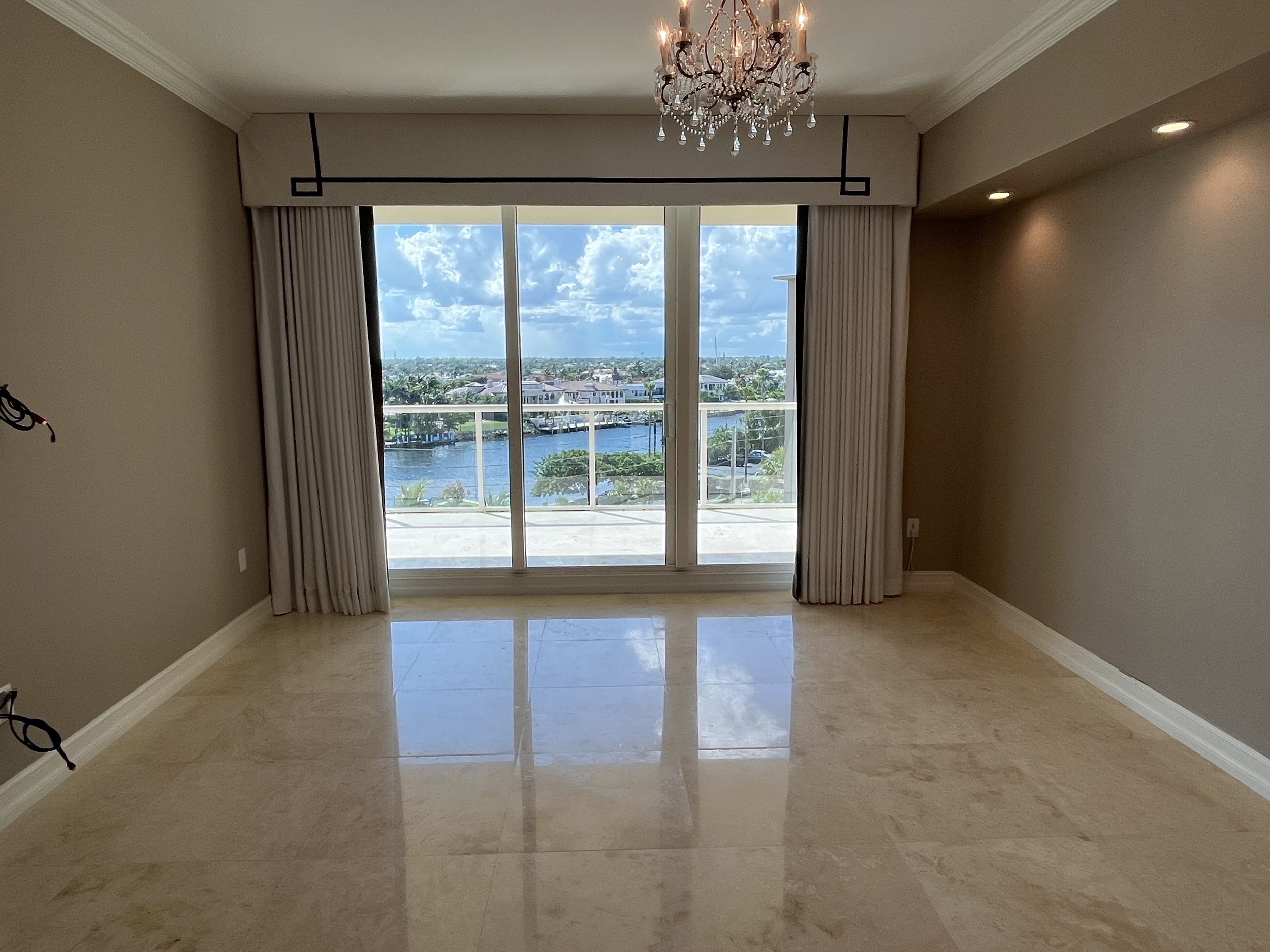 Before Hillsboro Beach condominium primary bedroom with dated finishes, polished stone flooring, traditional window treatments, and an underutilized waterfront layout before luxury renovation.