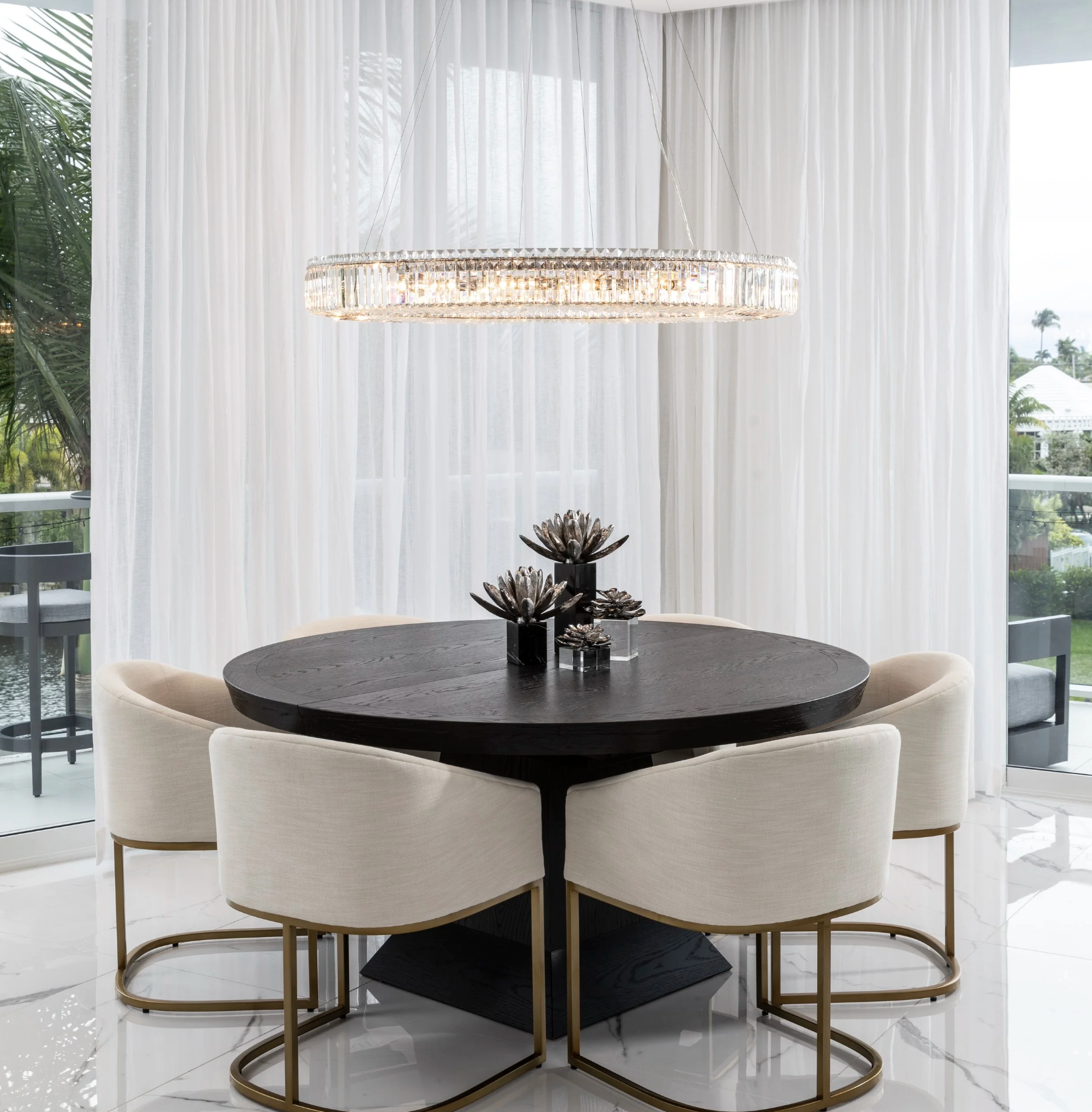 Fort Lauderdale penthouse dining area with a round wood table, upholstered seating, crystal ring pendant, and white linen drapery, designed for sophisticated client dinners and intimate entertaining