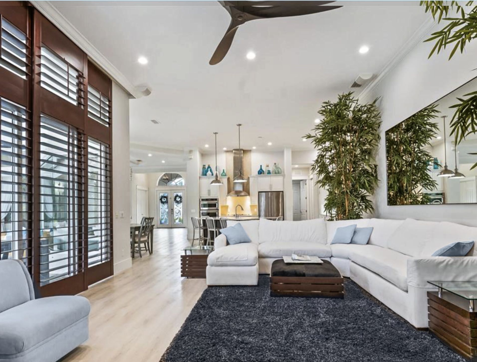 Luxury family room decorating in Lakewood Ranch featuring a white sectional sofa, custom haircalf storage ottoman on hidden casters, open-slat end tables, and dark wood Hunter Douglas plantation shutters.