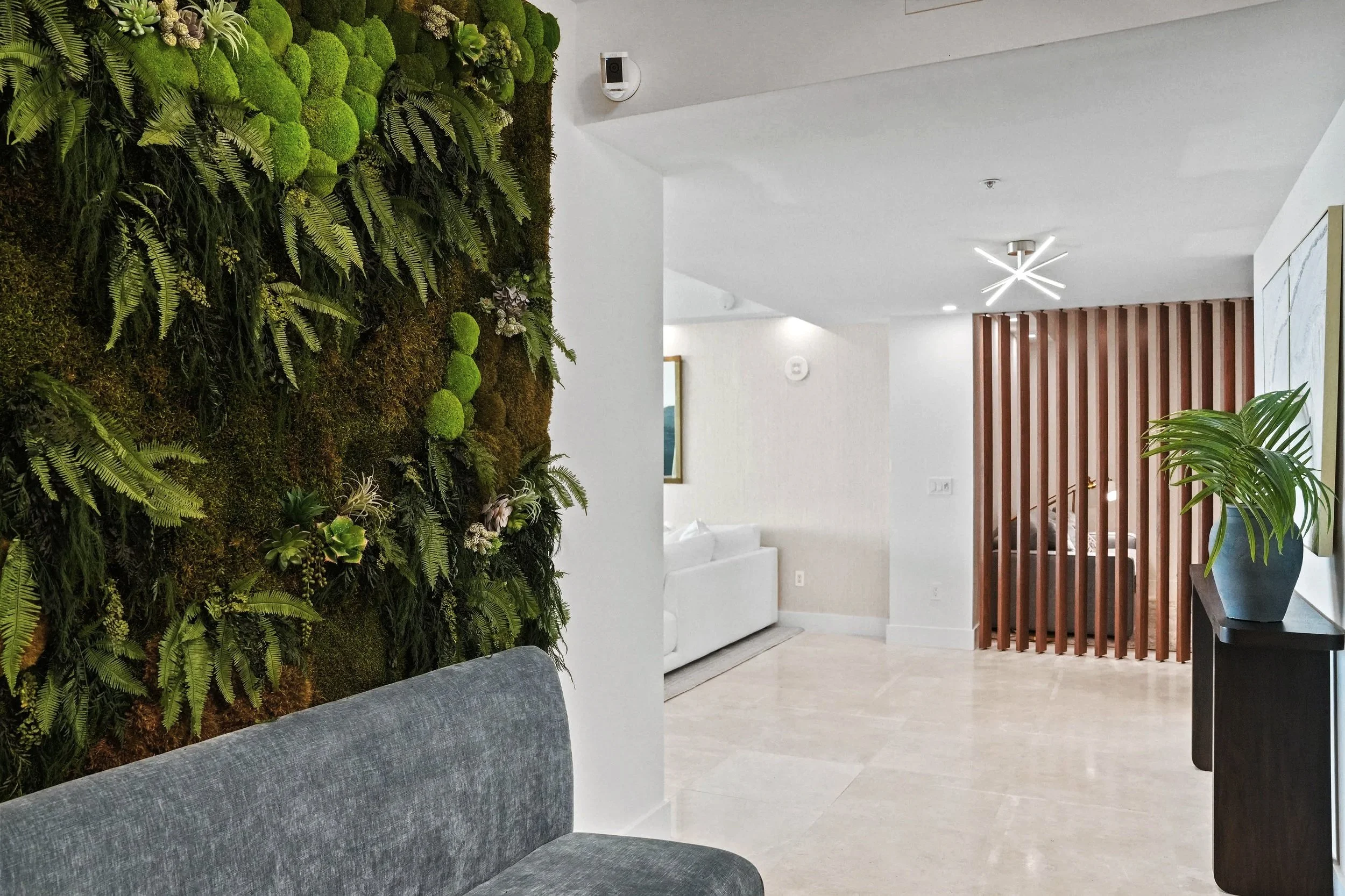 Luxury Hillsboro Beach condominium entry featuring a custom preserved green wall, open wood slat partition, contemporary lighting, and warm modern coastal interior design by Exclusively To Design.