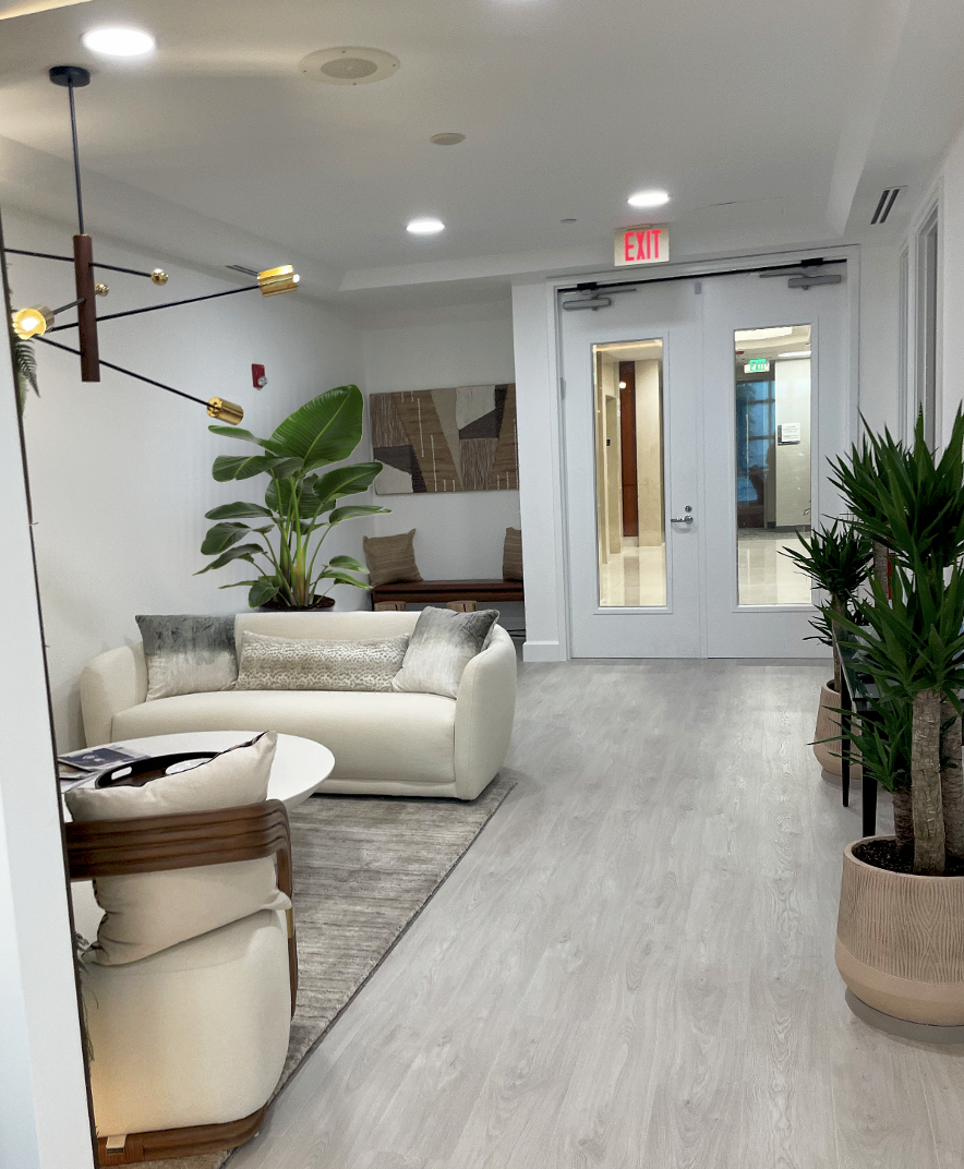 Updated law firm lounge designed by Exclusively to Design featuring a soft pale grey performance laminate flooring, an open seating lounge with curved sofa and a feature biophilic green signage wall.