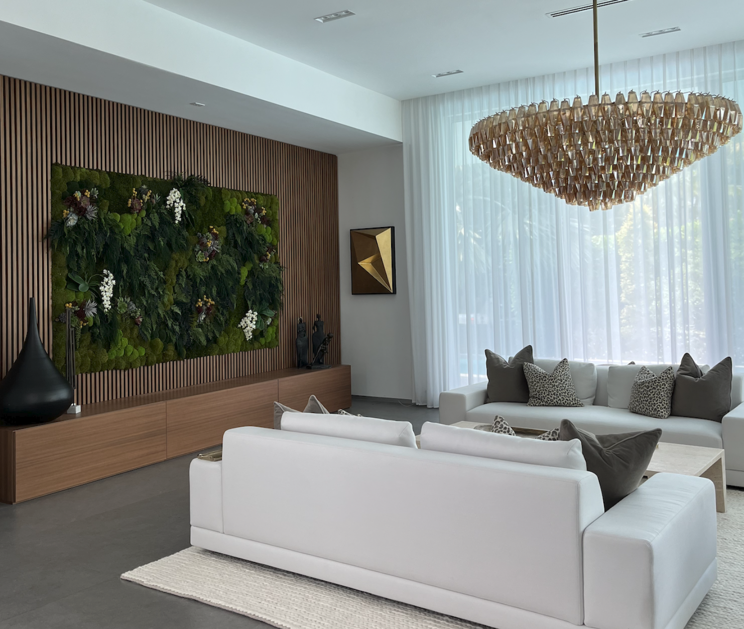 Miami Beach living room with sculptural chandelier, white seating, and biophilic wall installation
