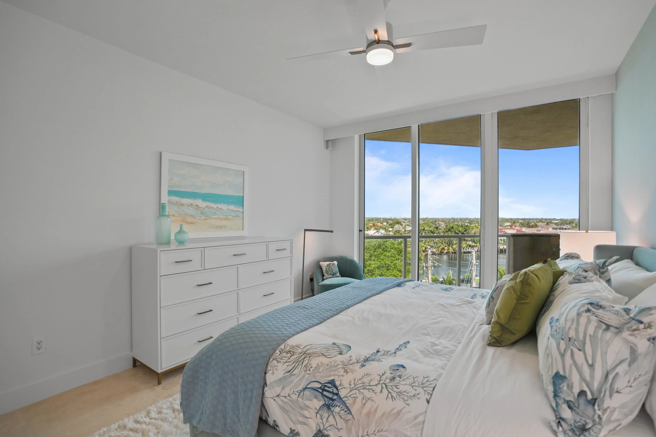 After aqua coastal guest bedroom in a Hillsboro Beach luxury condominium featuring custom coastal furnishings, layered blue and white bedding, waterfront views, and a tranquil retreat for family and guests.