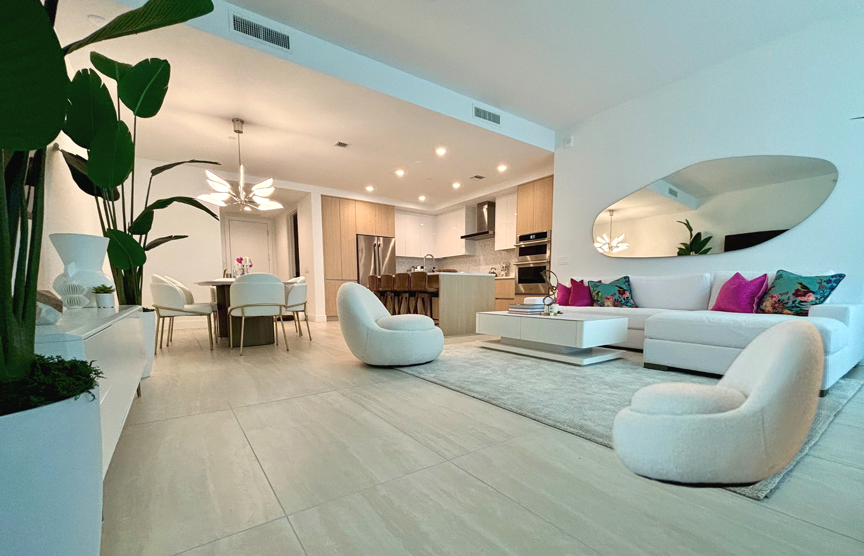 Luxury condominium interior design at The Baso in downtown Sarasota by Exclusively to Design featuring a white linen sectional sofa with magenta and teal pillows, curved boucle swivel chairs, and an open kitchen layout.