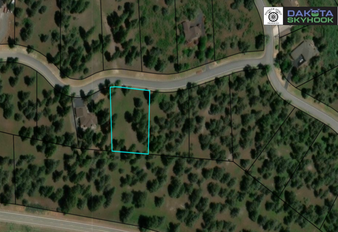 Aerial view of a wooded residential area with a highlighted plot of land outlined in blue, showing a house and trees, near a winding road.