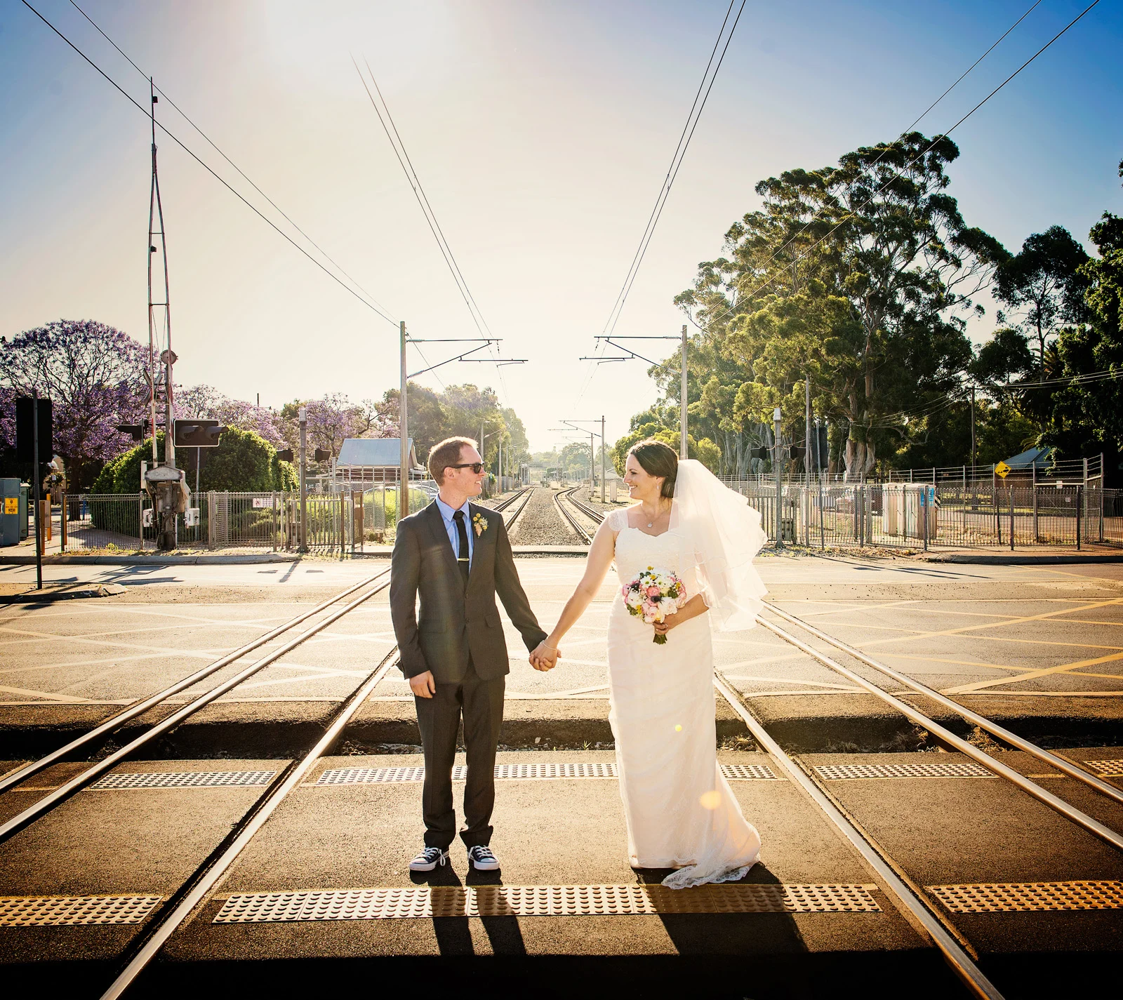bride and groom standing apart while holding hands in middle of railway tracks, Guildford.