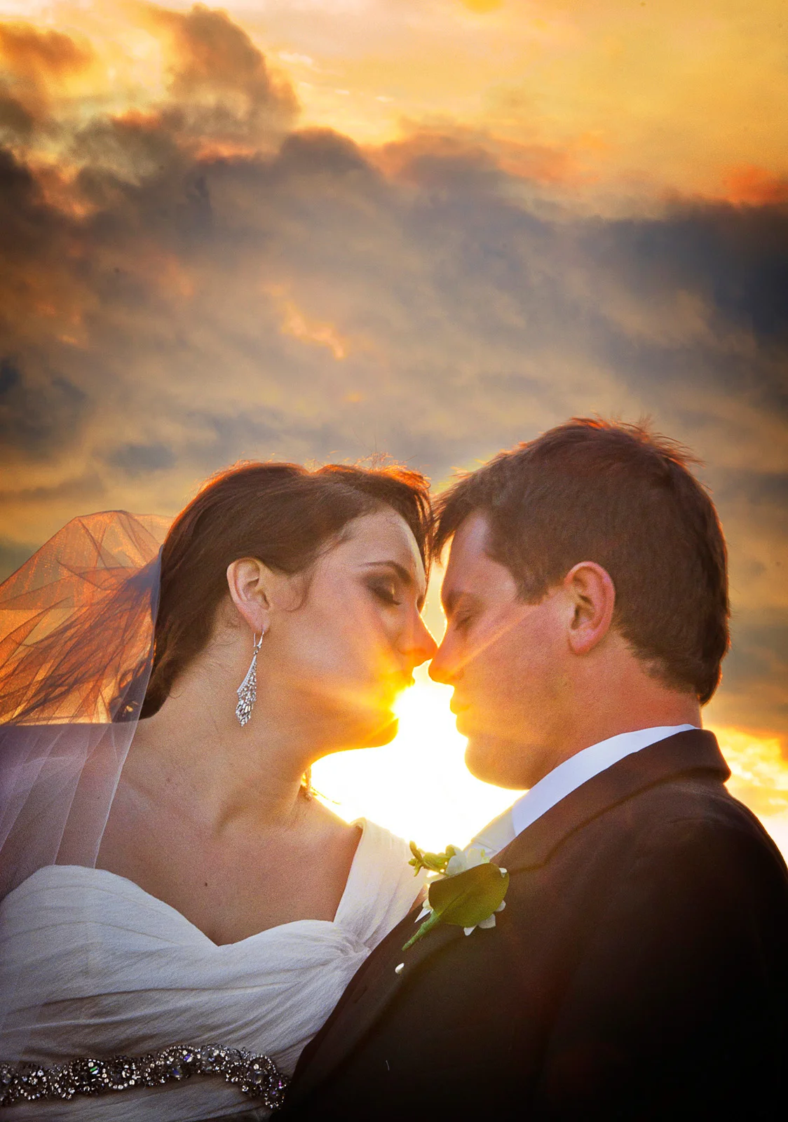 Married couple touching noses with sunset shining through gap