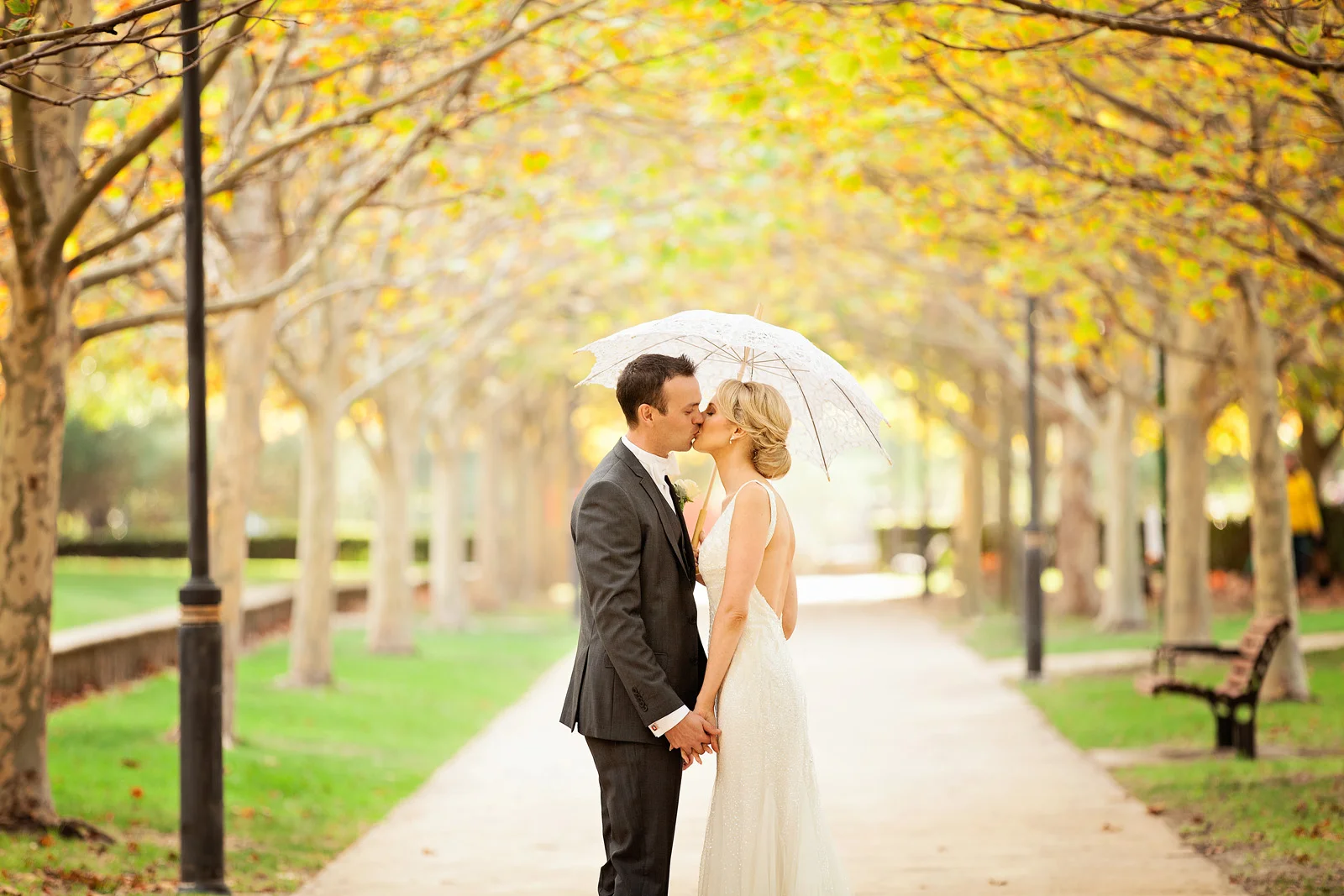 Newlyweds kissing under a parasol in a park during Autumn at Subiaco Common.