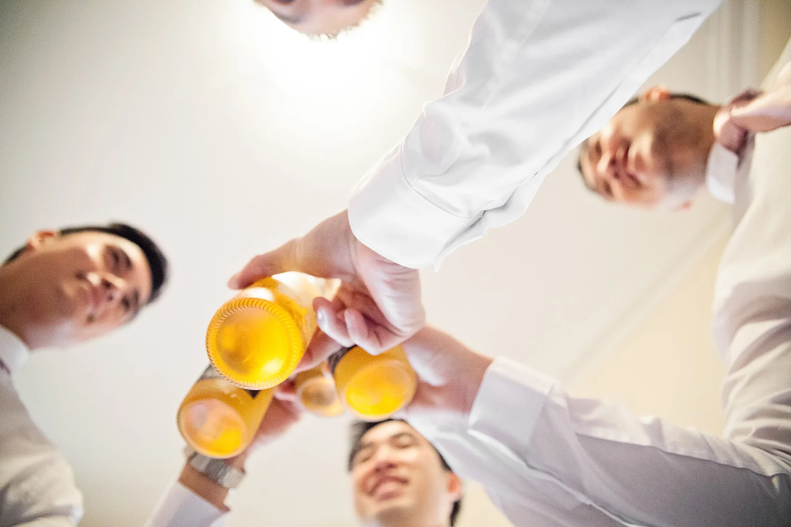 Close up from below looking up of Groomsmen clinking beers.