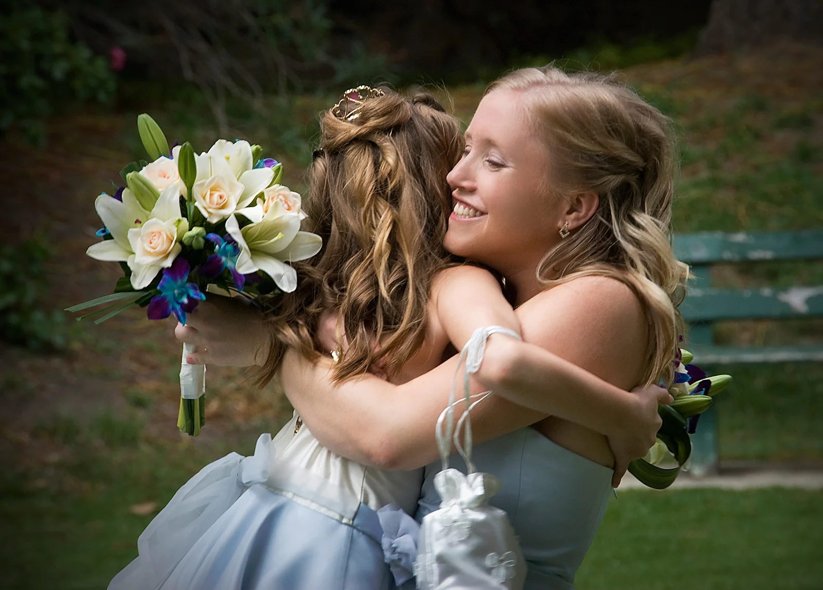 Bride lovingly embracing flower girl outdoors on sunny day