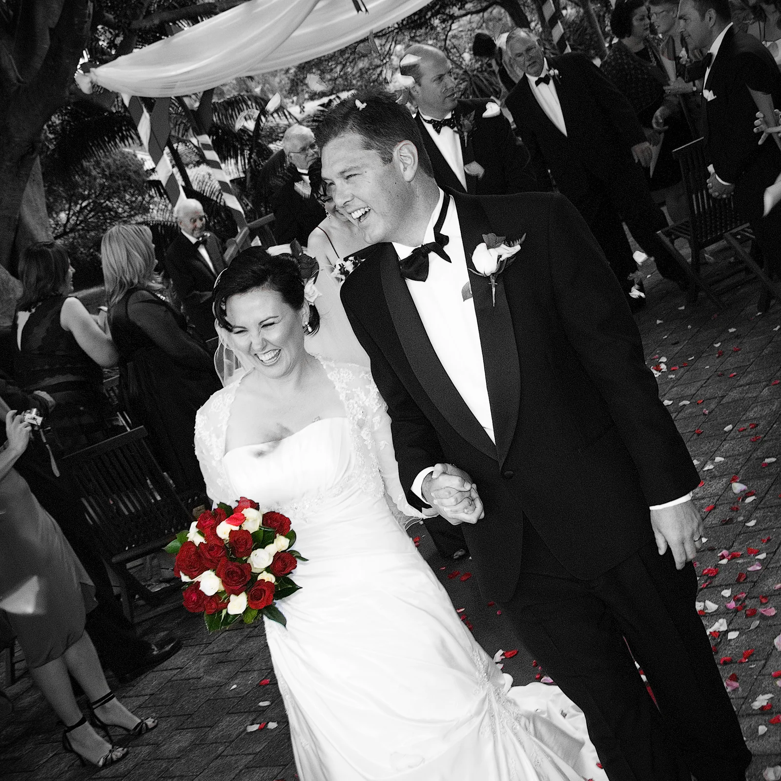 Smiling Bride and Groom walking down the aisle with red bouquet. Caves House, Yallingup