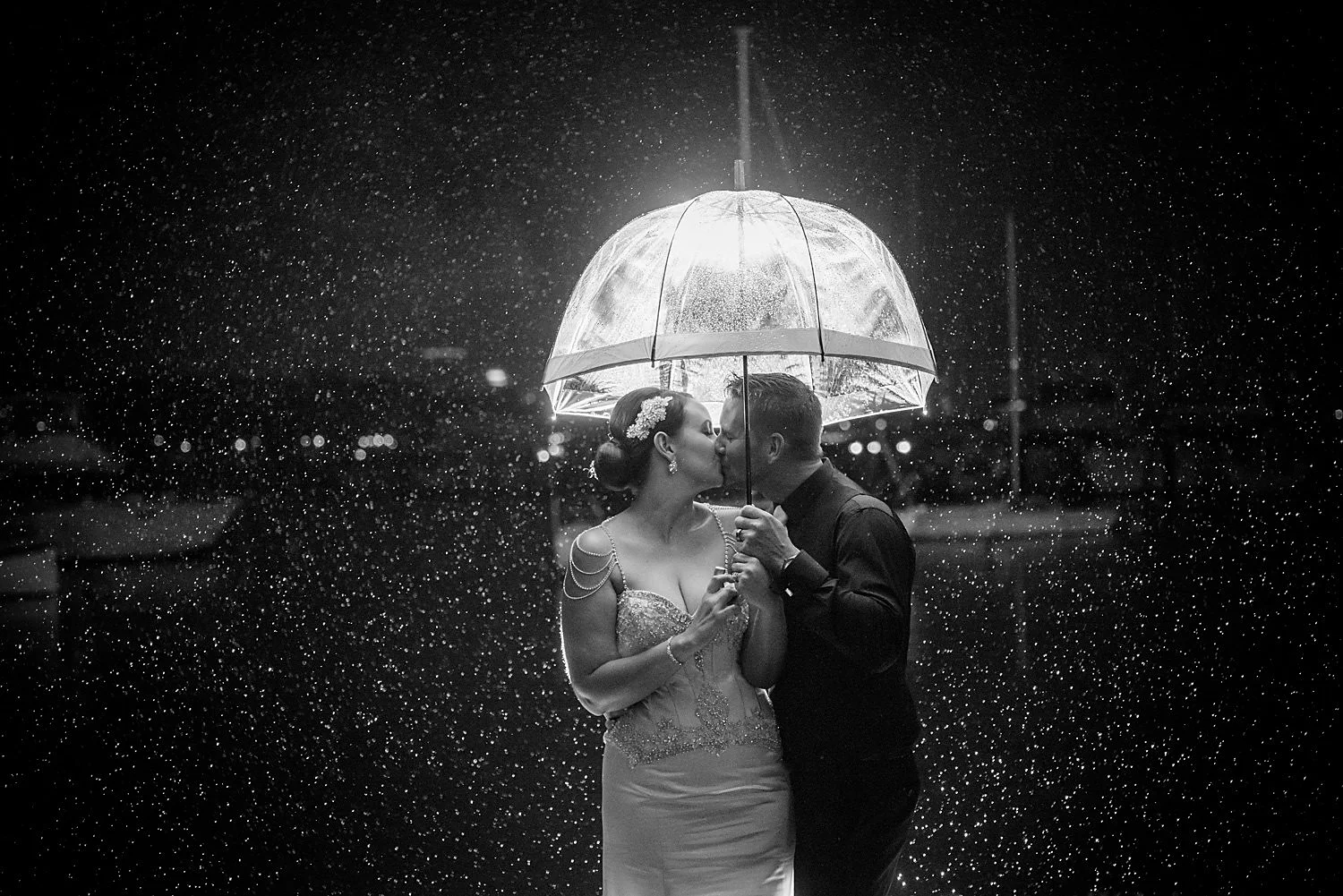 B&W image of couple kissing in the rain at night under an umbrella, Matilda Bay.