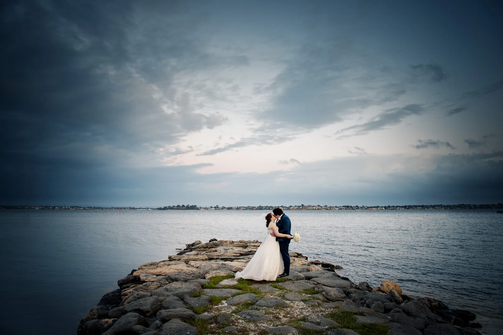 Bride and Groom kissing on Rocky jetty during stormy evening, JoJo cafe Nedlands