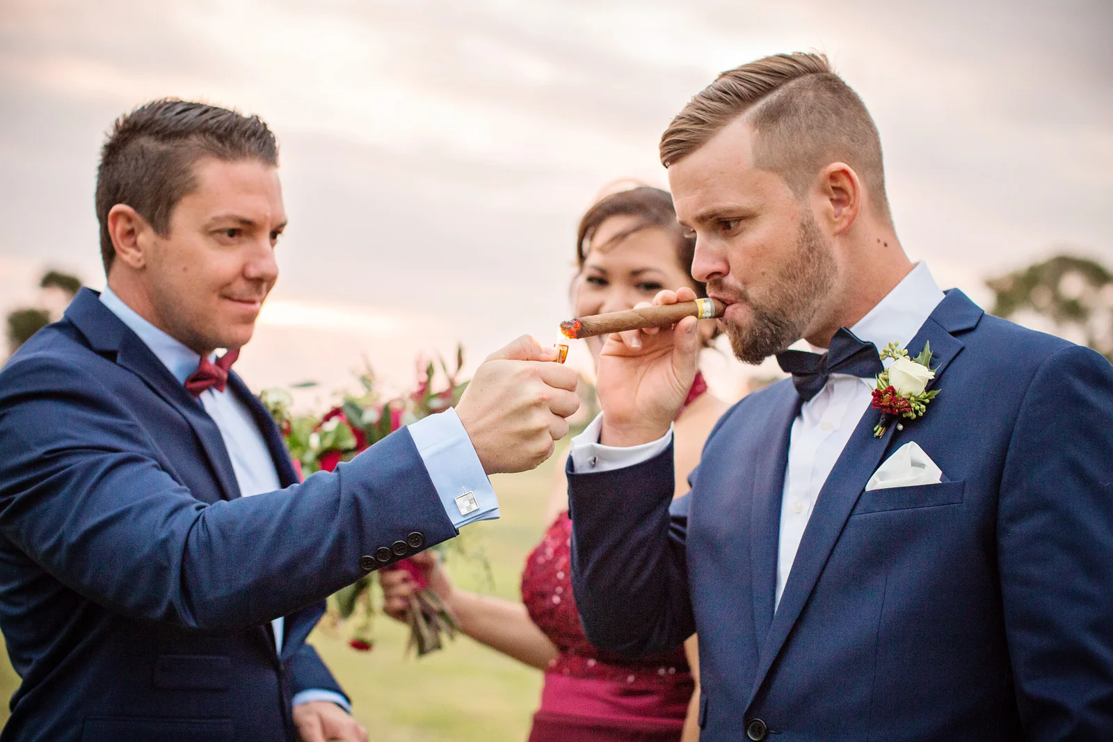 Groom celebrating by smoking a cigar lit by Best Man