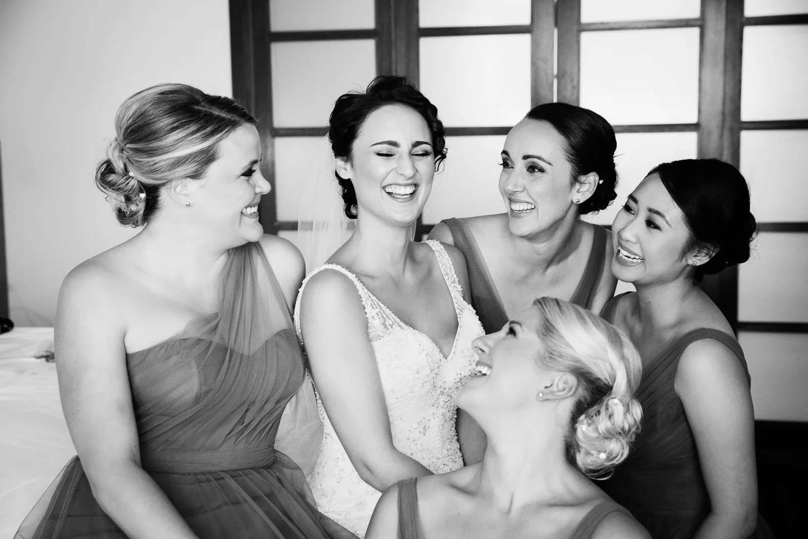 Bridesmaids laughing together while sitting on the bed at home