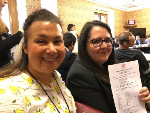 How Do I COO Taryl Law and Digital Marketing and Project Assistant Zeinab Ali smiling for the camera and holding up their invite to the roundtable