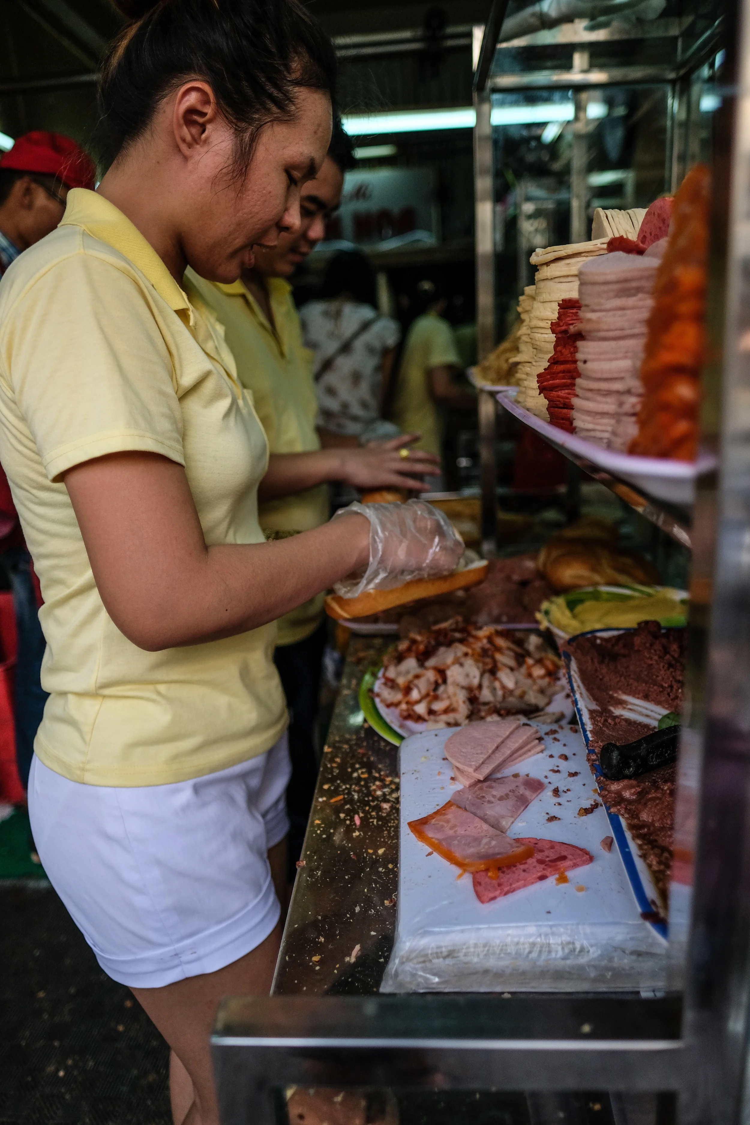 Preparing Banh Mi at the tiny but famous Banh Mi Huynh Hoa on Le Thi Rieng. It is a term for all sorts of bread, but is also used for the typical Vietnamese baguette with a variety of meats, a spread of pate, herbs and chillies.