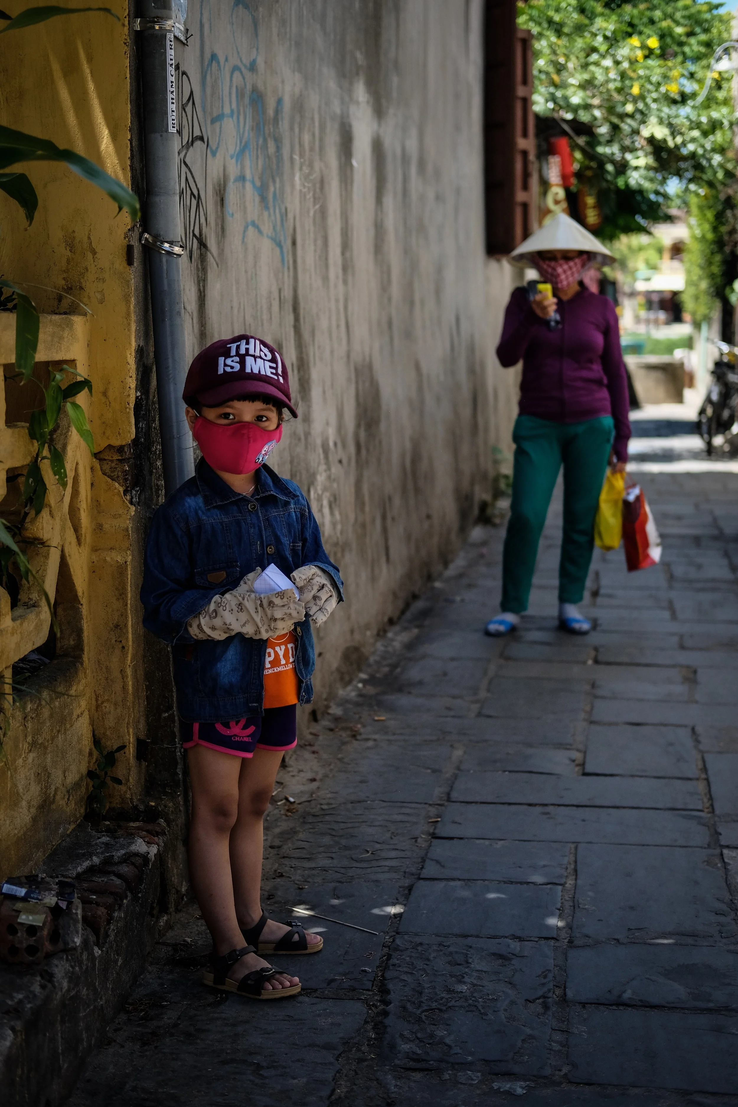 Having a look at the touris while mom checks her phone. The face masks are ubiquitous in Vietnam, and are mostly for protection against the sun, people try to keep their skin as light as possible. 