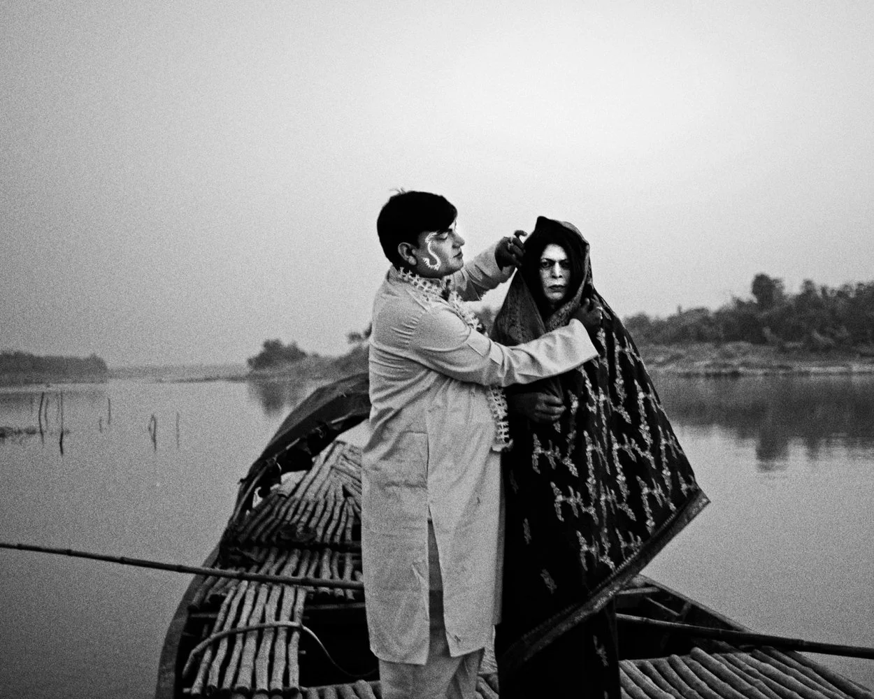A black and white photo of a man helping a woman on a boat near a calm river with trees in the background.