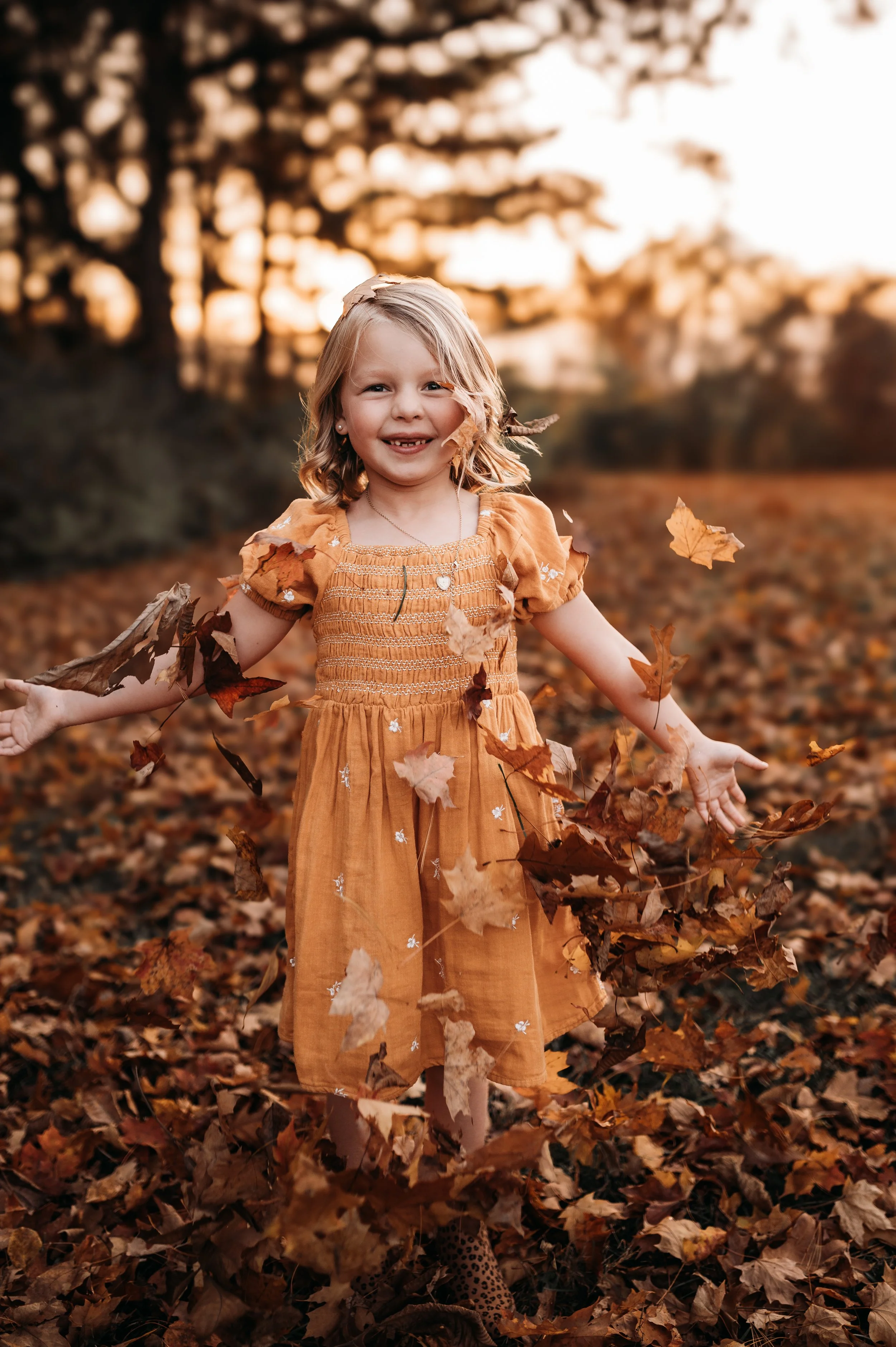 Girl standing in golden fall leaves smiling for a photo
