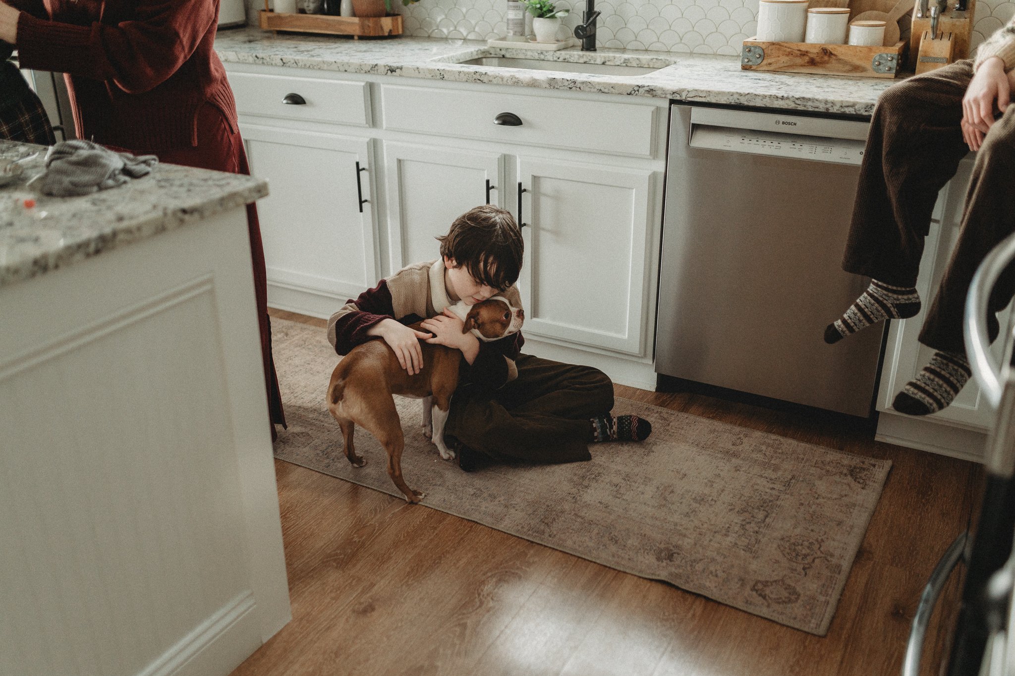 Boy cuddles his dog on the kitchen floor 