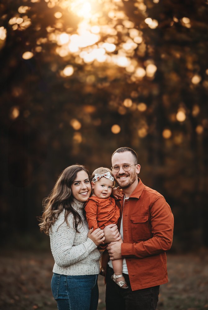 Family with young toddler posing with the golden fall leaves at sunset