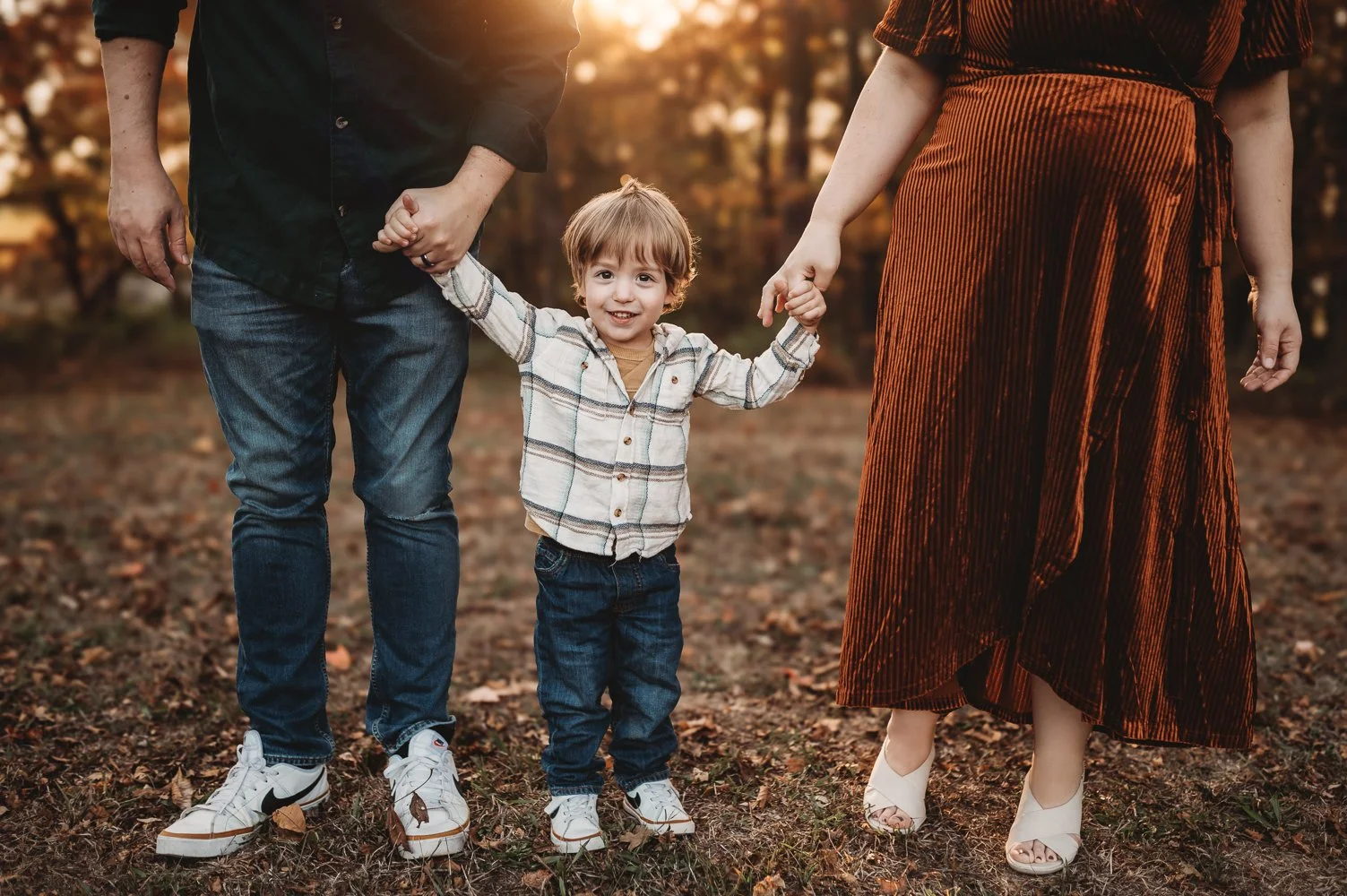 Photo of a toddler in the golden fall leaves at sunset for a family photo