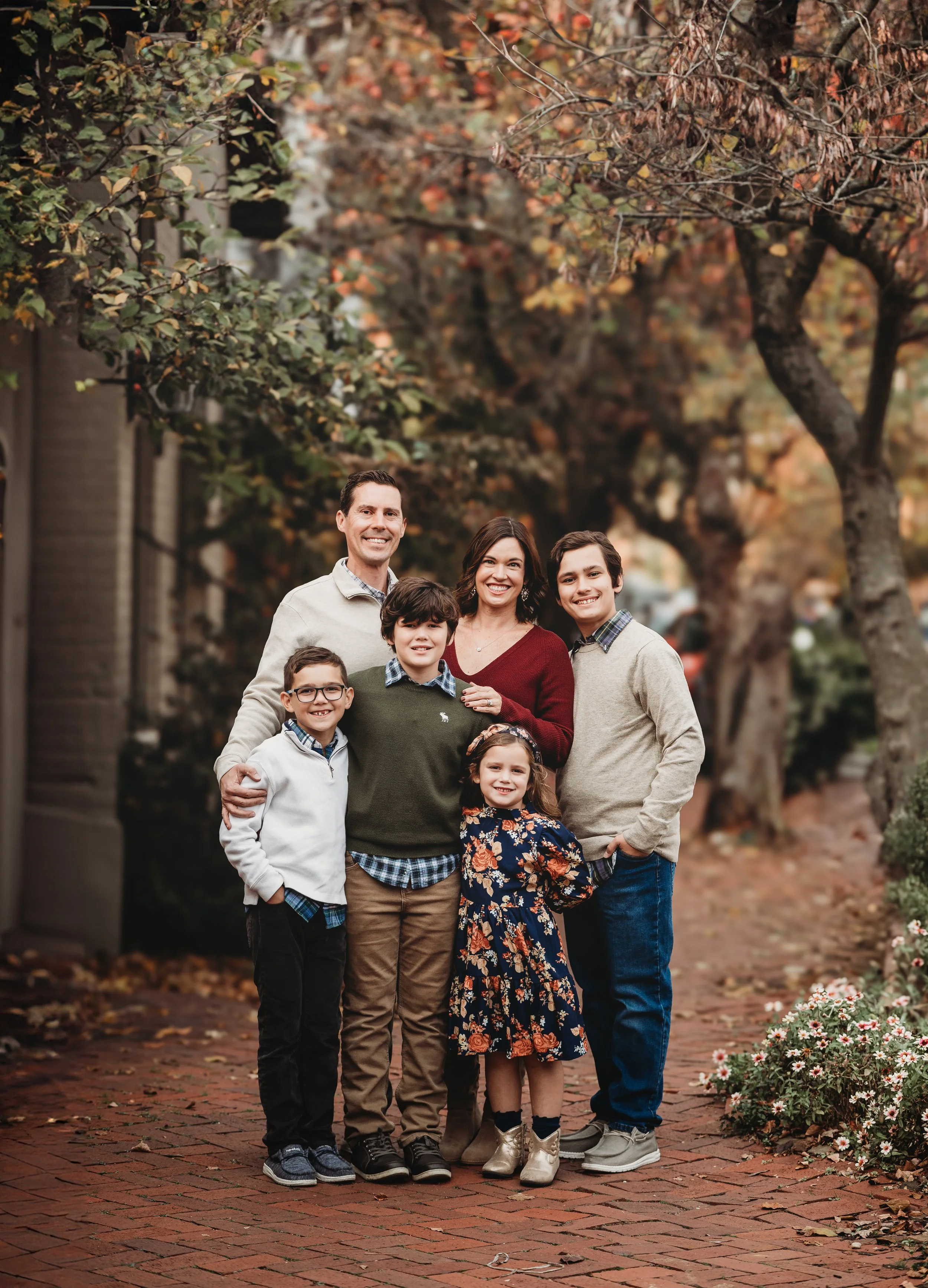 Family of six standing together on a brick sidewalk in the fall scenery for a family photo
