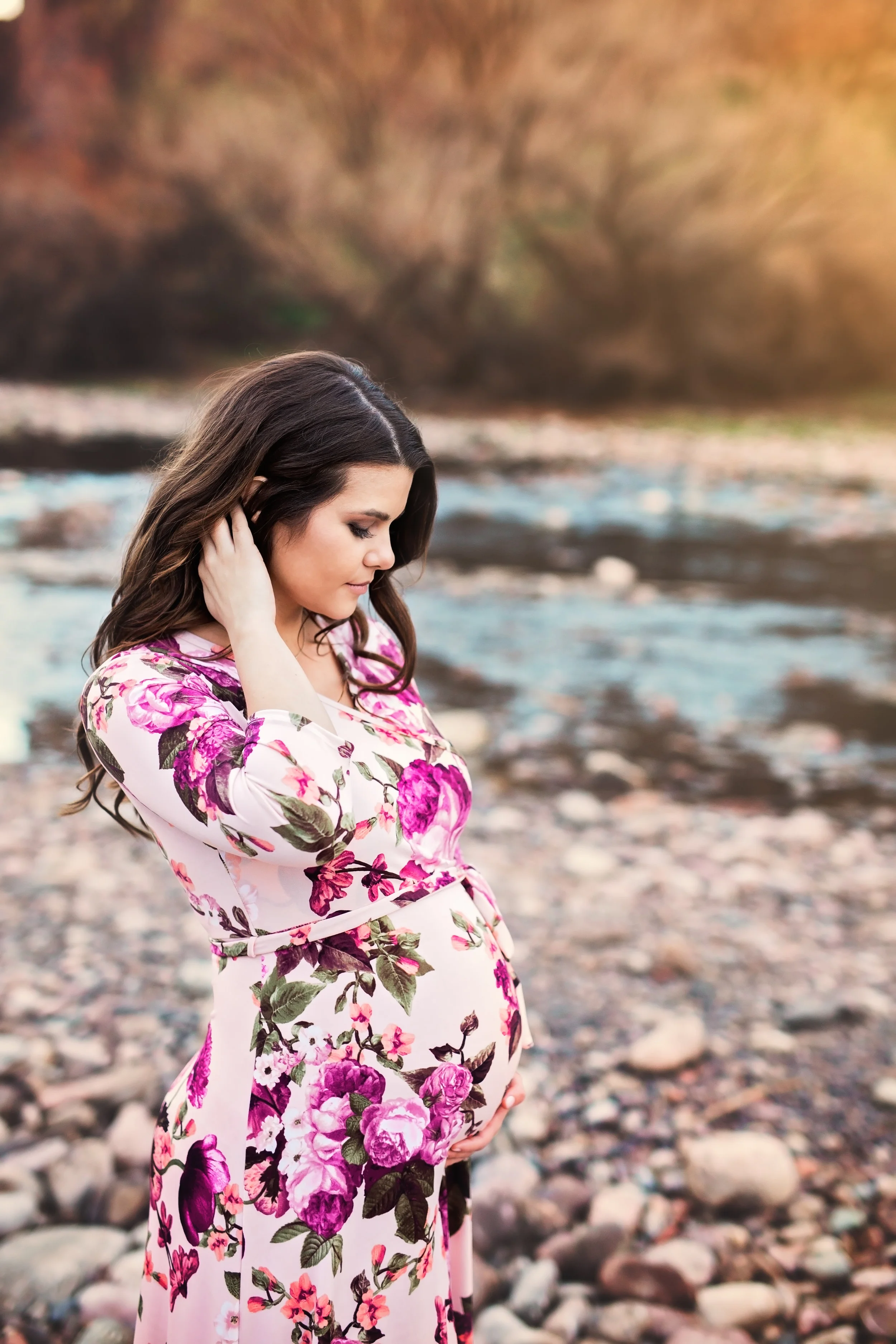 Pregnant woman in floral dress posing alongside creek during Maternity Session